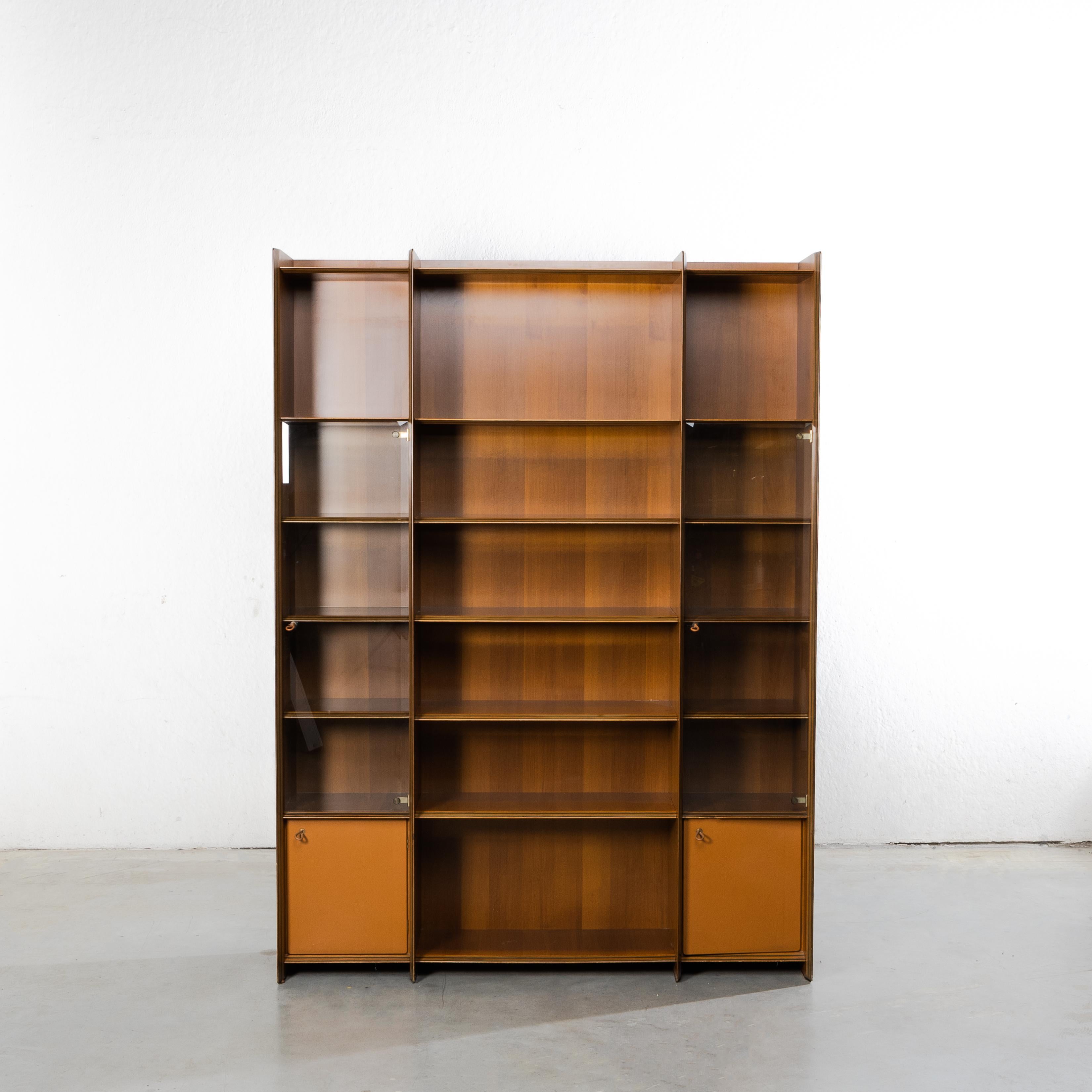 Bookcase, showcase in walnut veneered laminate.
Stiles and shelves made of layers of walnut and hardwood in contrasting colors.
The cabinet includes open storage spaces.
Two spaces closed by a bevelled glass with leather handle on the left and on