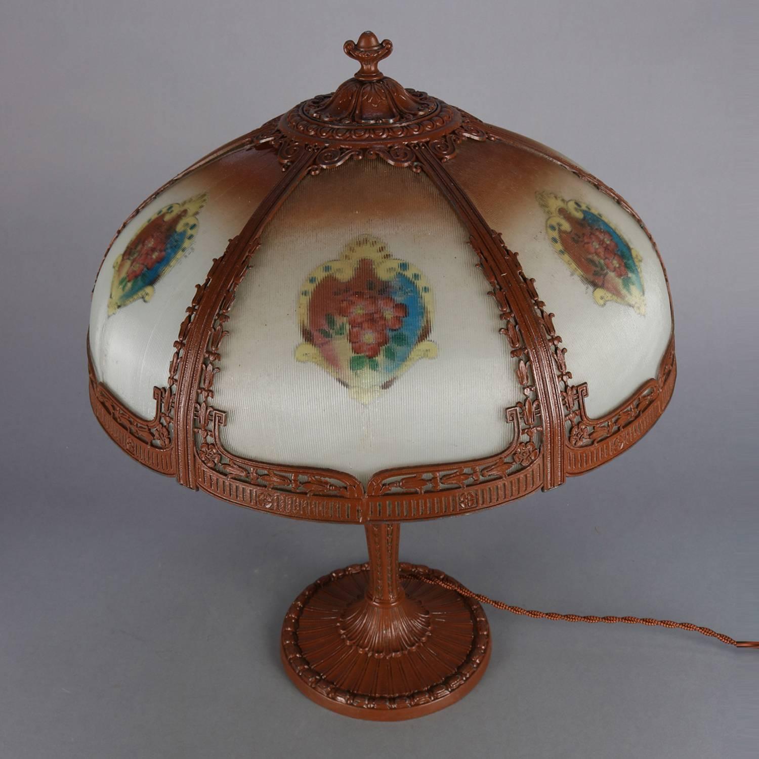 Arts & Crafts antique Pittsburgh School table lamp features cast reeded base with graduated bellflowers, six-panel reverse painted shade features frame with pierced floral decoration and containing floral hand painted ribbed glass panels, circa