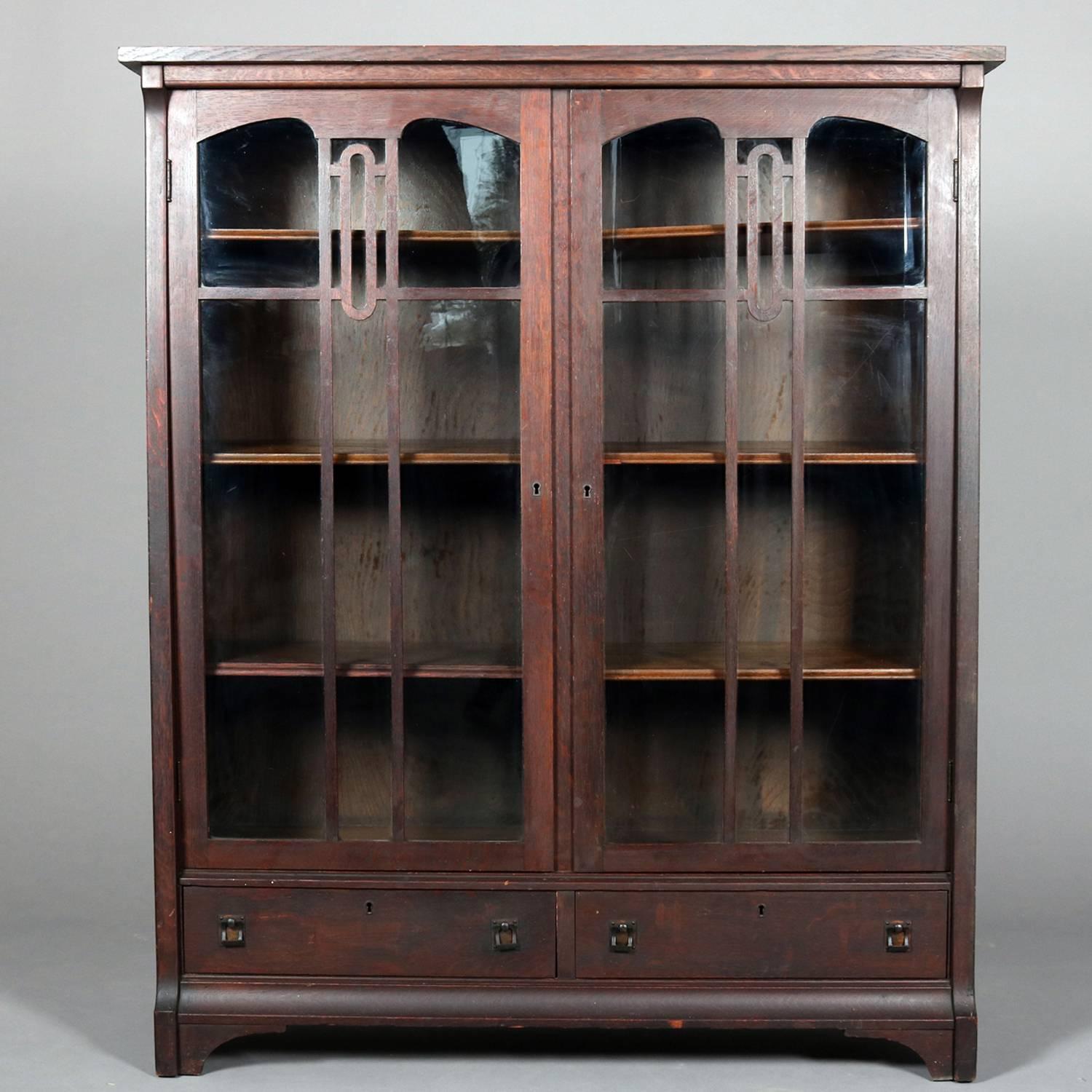 Arts & Crafts Gustav Stickley School mission oak bookcase features simple form with two glass door opening to adjustable shelf interior over two drawers, bronze pulls, circa 1910.

Measures: 56
