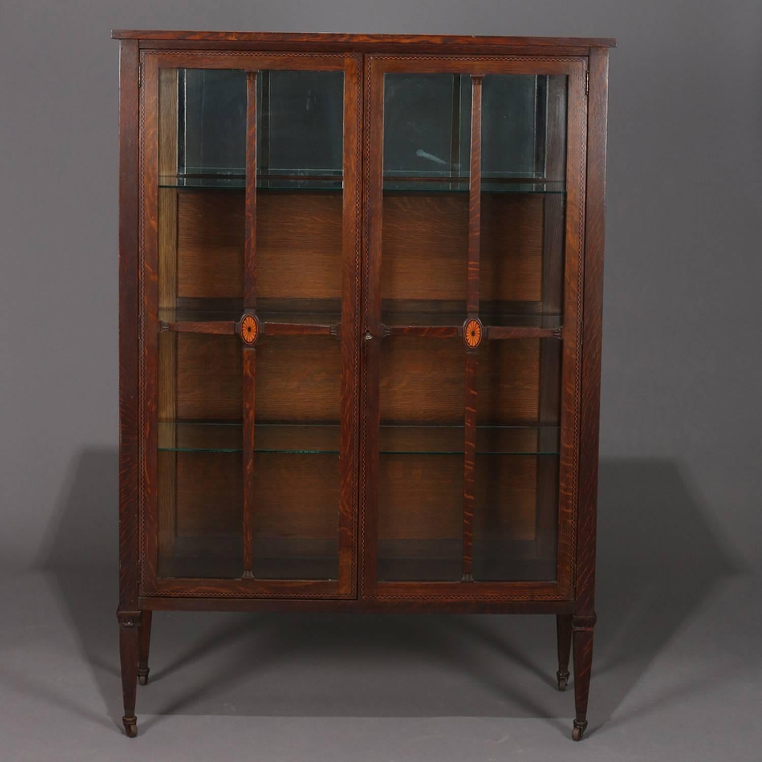 Arts & Crafts mission oak two-door china cabinet by Lifetime Furniture Co. of Grand Rapids, MI features oak construction with ebonized and satinwood banding and patera medallions, two glass doors with lock open to a mirrored and fixed shelf