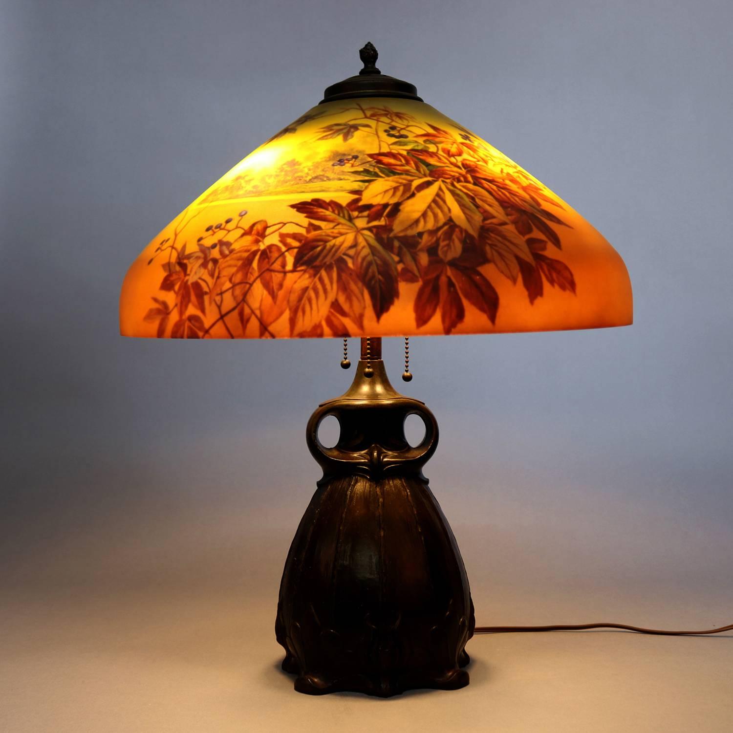 Antique Arts & Crafts table lamp by Handel features double hand vessel form cast base with three lights and Pittsburgh School reverse painted shade depicting lake scene and foliate overlay, handel lamps label on base, circa 1920.

Measures: 24