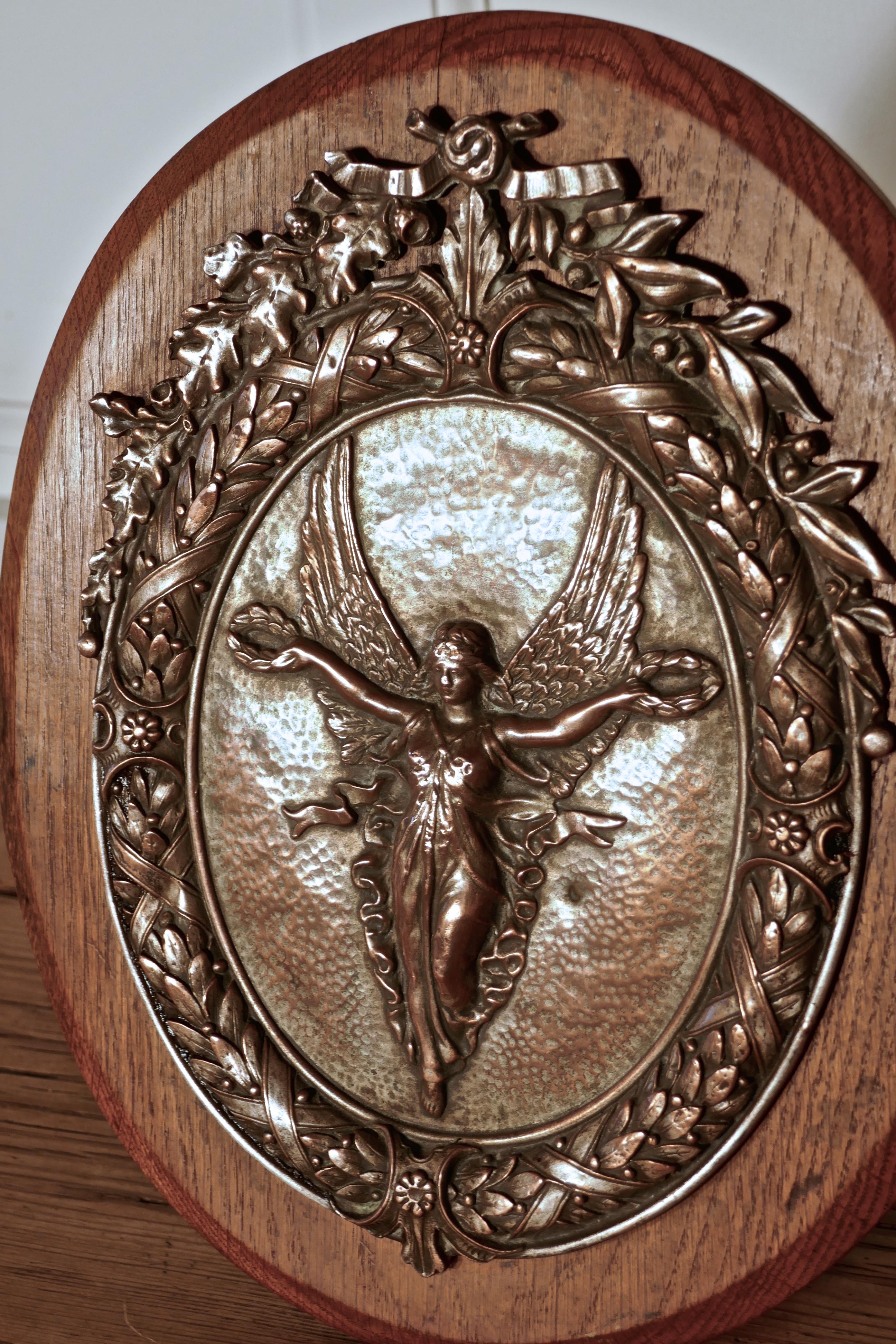 Arts and Crafts 19th Century Shield Trophy with Nike the Goddess of Victory 

The is an Arts and Crafts piece, the Oval Oak shield has an embossed Coper plated mount, in the centre there is an oval cartouche with the Nike the Winged Greek Goddess