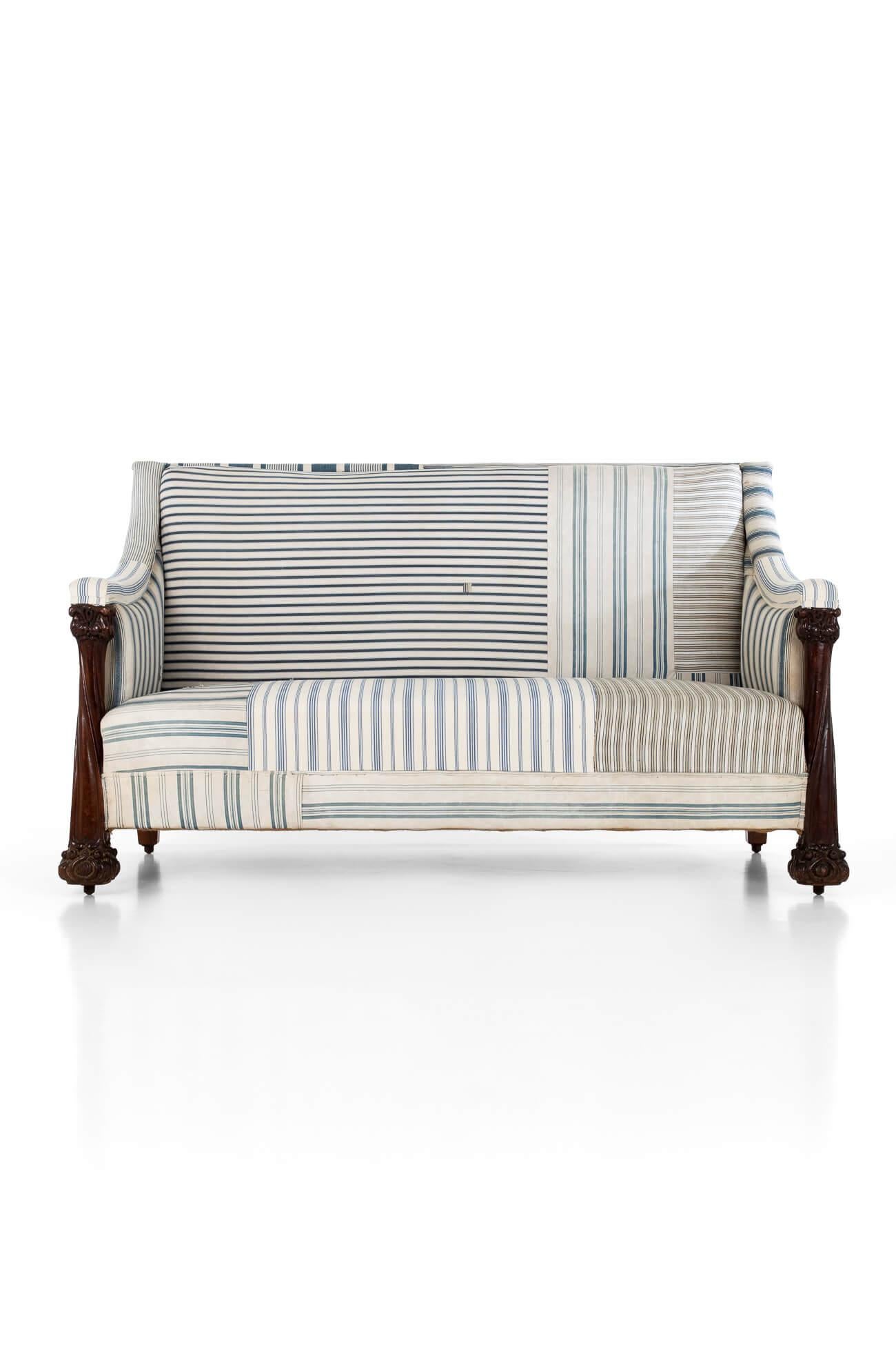 A wonderful and unique Arts and Crafts sofa in original blue stripe ticking upholstery.

With a generous straight back, accompanied by gently scrolled padded arms that lead to two large carved mahogany pillar arm supports.

Beautifully carved