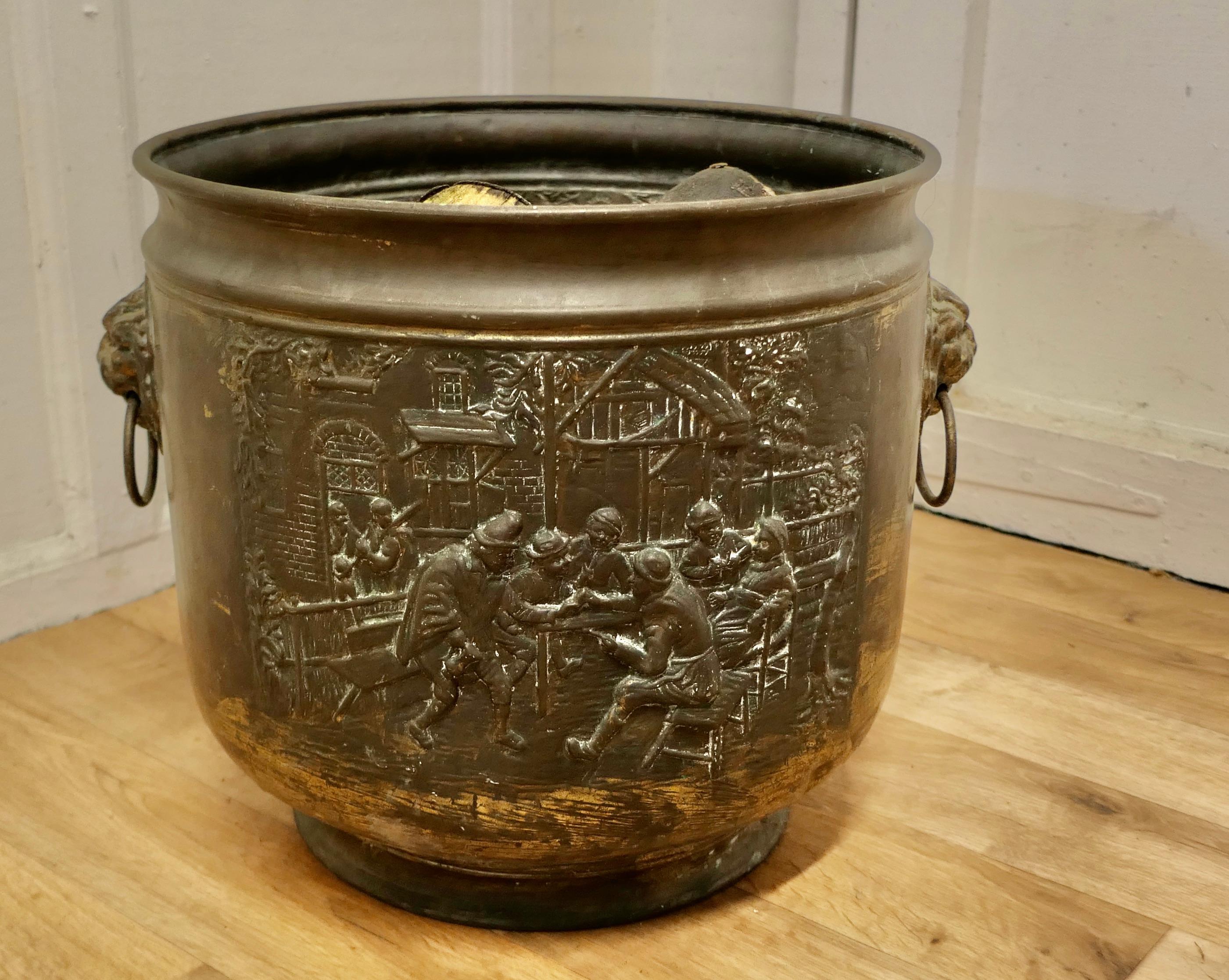 Arts and crafts brass log or coal bin, with tavern scenes 

This is a lovely old cauldron it sits on a brass plinth with Lions mask ring handles at each side, the bucket is made in beaten brass and has embossed Tavern and Country scenes around the