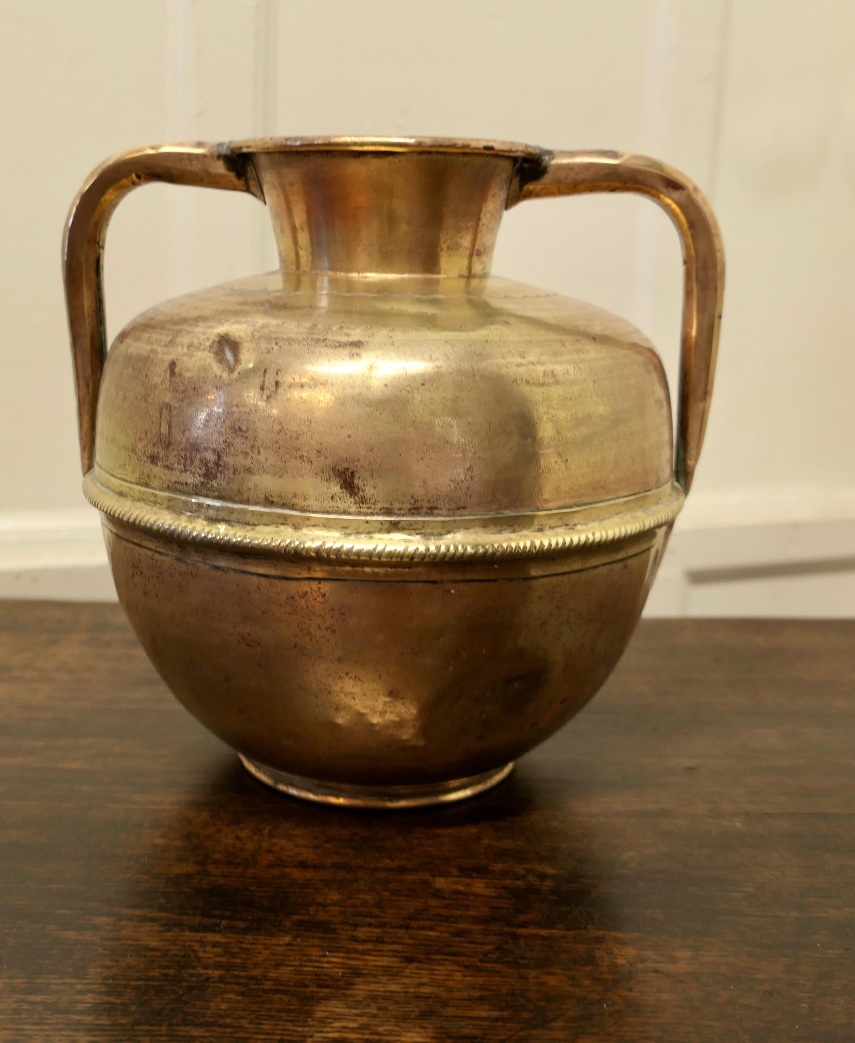 Arts and Crafts brass urn with handles.

A lovely old piece, in solid beaten brass, the vase has a “Pot Belly” shape with 2 jug handles at the top.
The vase in used condition with a few dents and lots of character, it is 11” high and 11” in