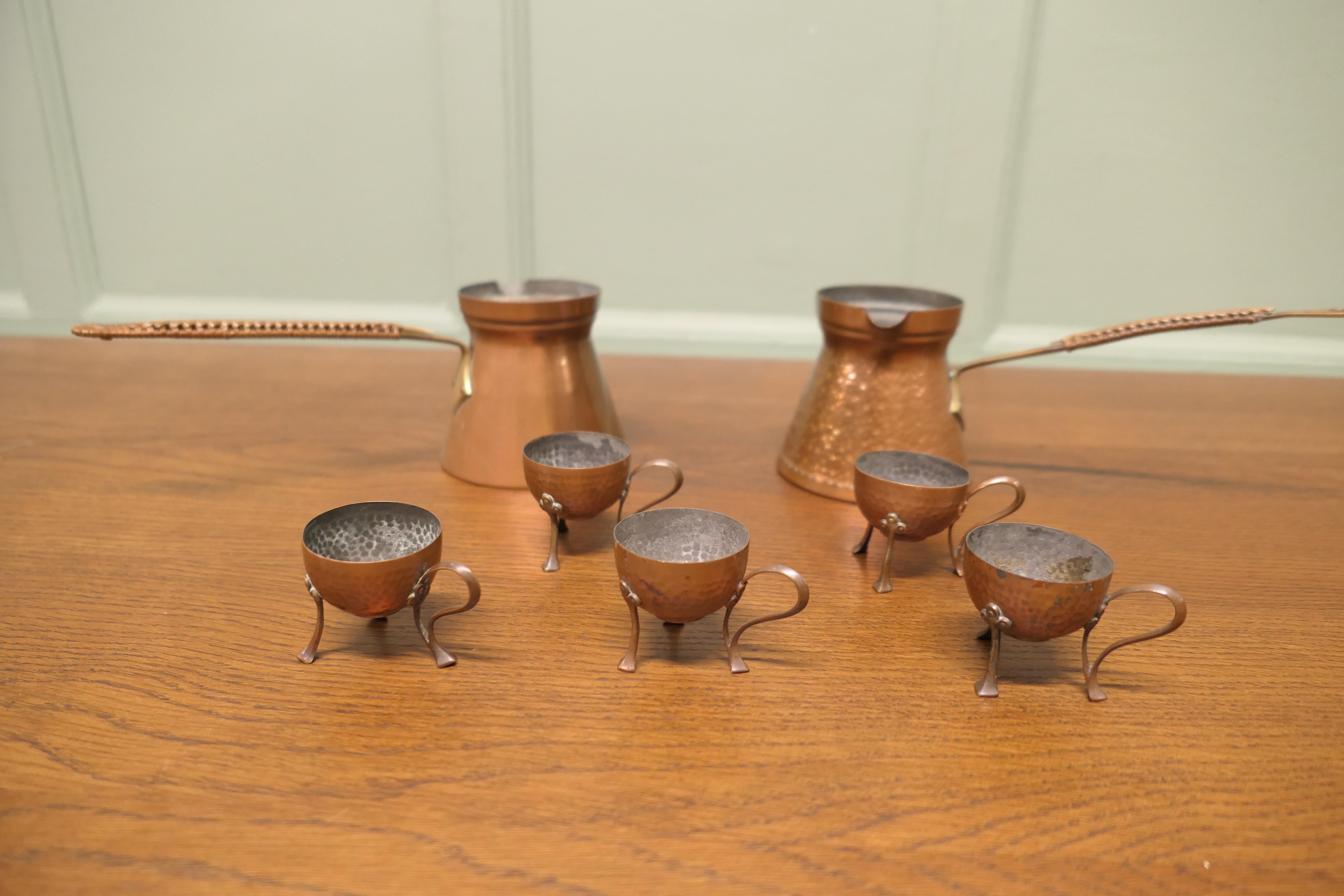 Collection'S di Arts and Craft in rame per la colazione

Una buona collezione di 5 portauovo in rame battuto a mano e 2 vasi di cioccolato, i portauovo poggiano su piccole gambe in ottone e i vasi di cioccolato hanno manici foderati di rafia