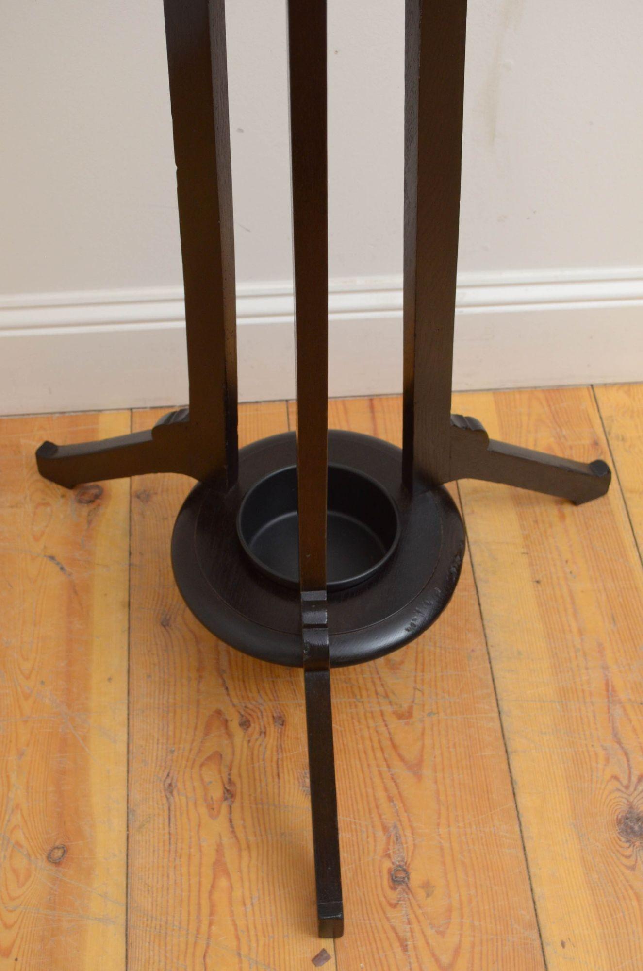 St029 Arts and Crafts ebonised oak hat stand, having brass hooks on revolving platform with finial to the top on 3 solid oak supports with further 3 brass hooks and brass umbrella holder, terminating in shaped legs and united by circular base with