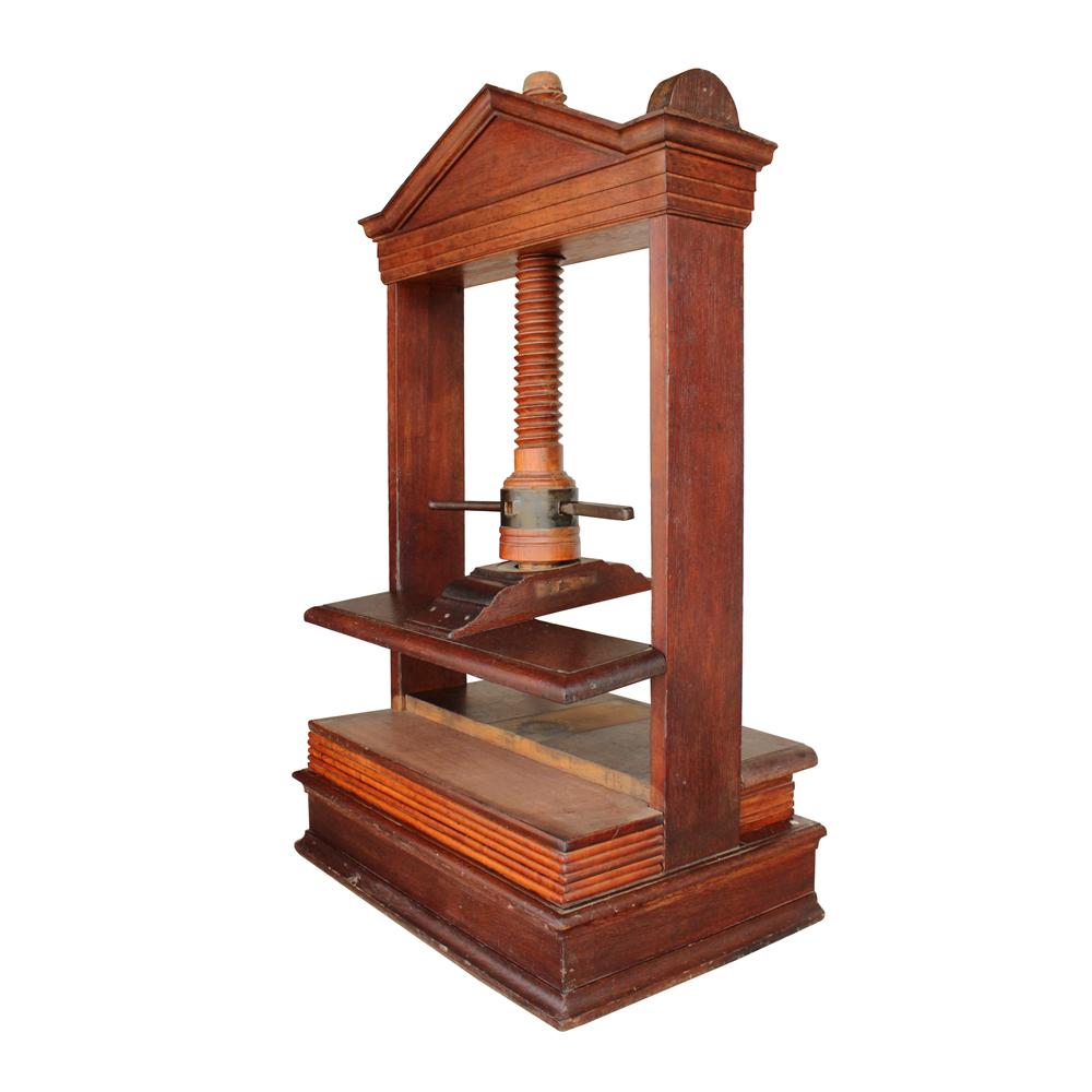 This gorgeous early 20th-century book press from the Boston area is composed of multiple beautiful hardwoods. The press is housed in a frame composed of a triangular pediment supported by pilasters. The shaft exhibits some checking with a few minor