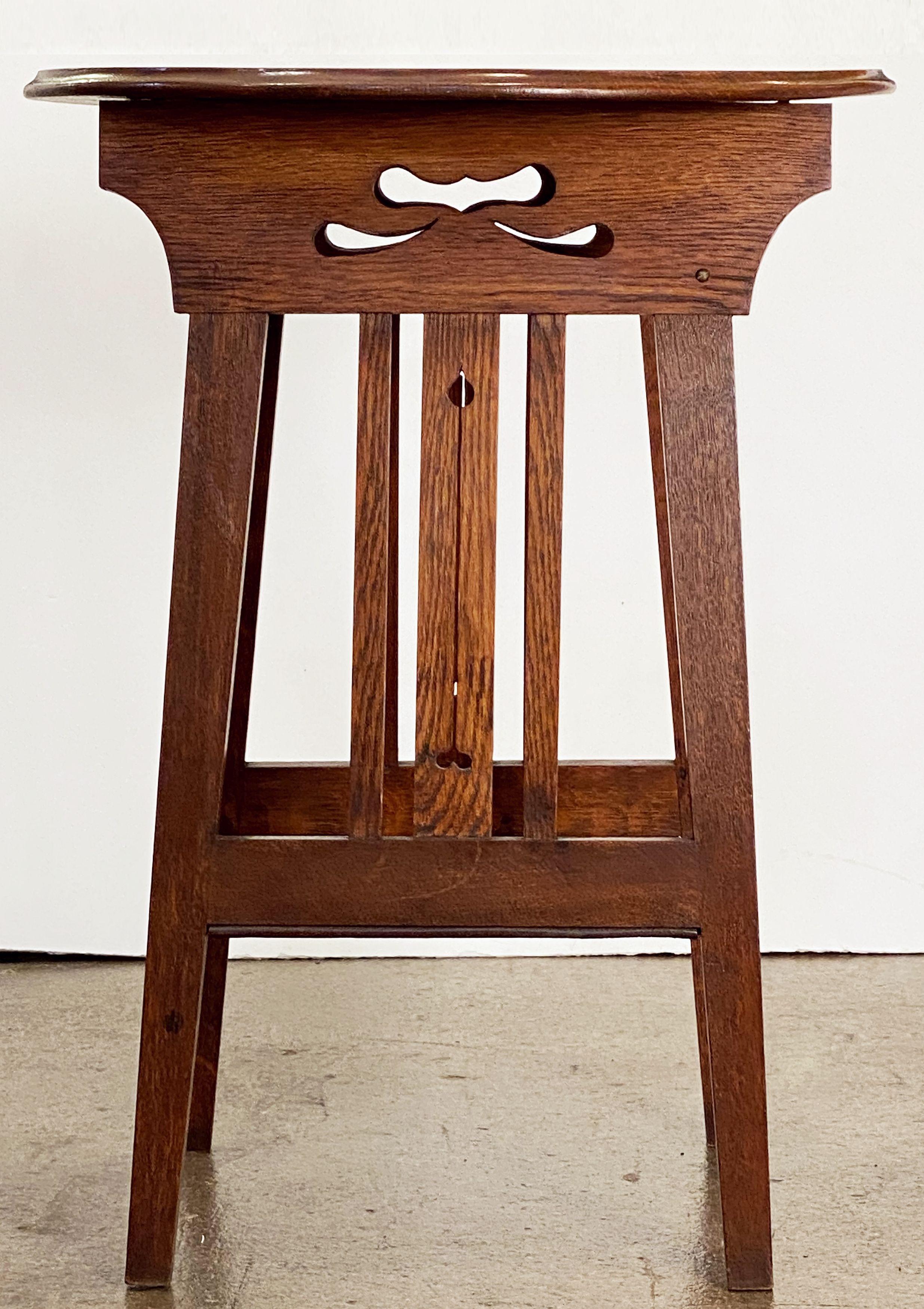 A fine English occasional or side table of oak from the Arts & Crafts Period, featuring a round or circular moulded top over a slatted, four-legged stretcher base with square bottom shelf. The slats with a distinctive Arts and Crafts cutaway design.