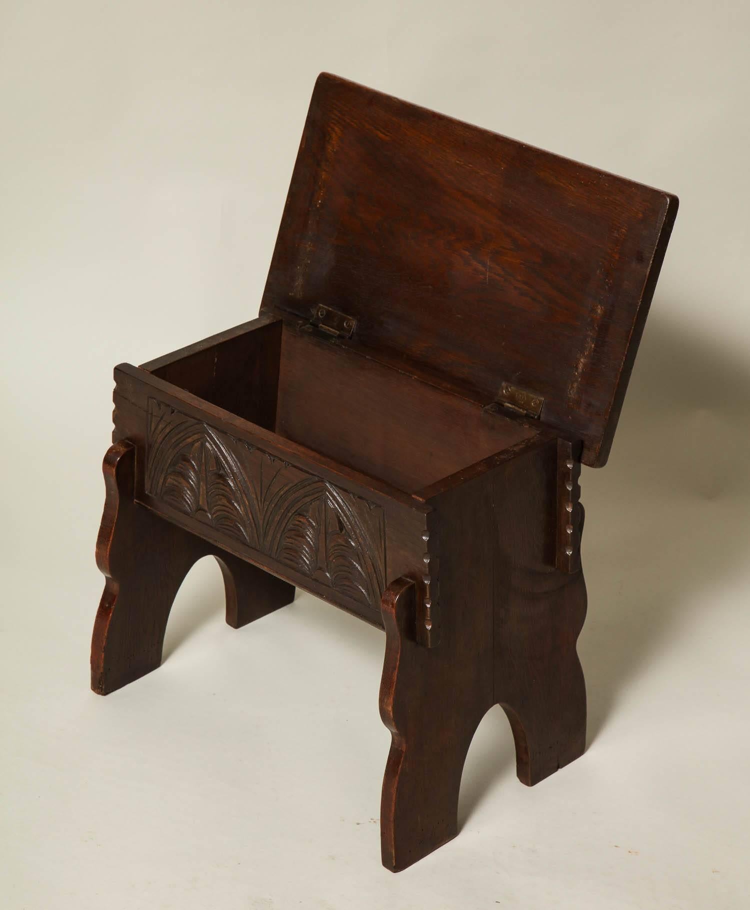 Good English Arts & Crafts period Gothic inspired stool, the hinged top over lunette carved apron, the splayed and arched legs notched to the front and back apron and having inset bottom, the whole with pleasing color and wear. Great as side table