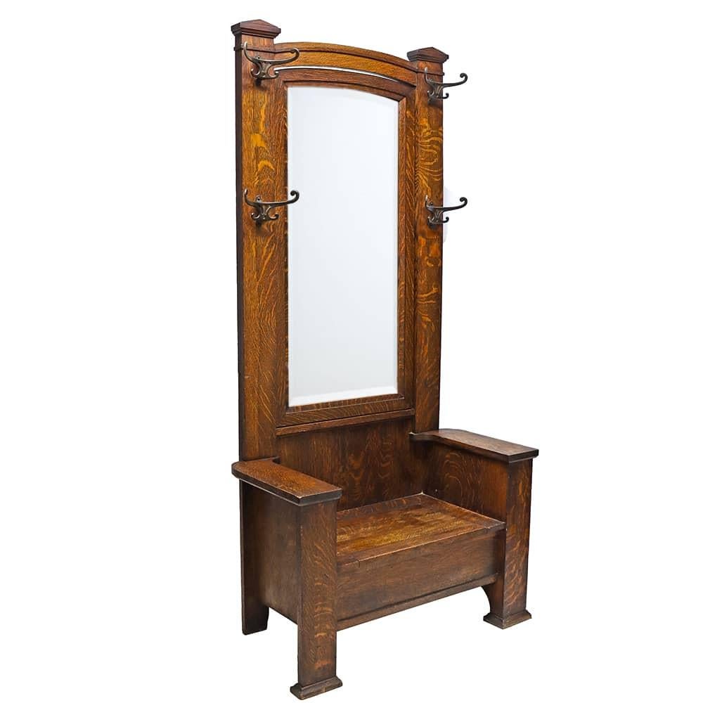 A stately solid oak hall tree with a Classic Arts & Crafts Silhouette. Elegant cast iron double hooks surround a beveled mirror at the center back and the bench seat flips up for some hidden storage.