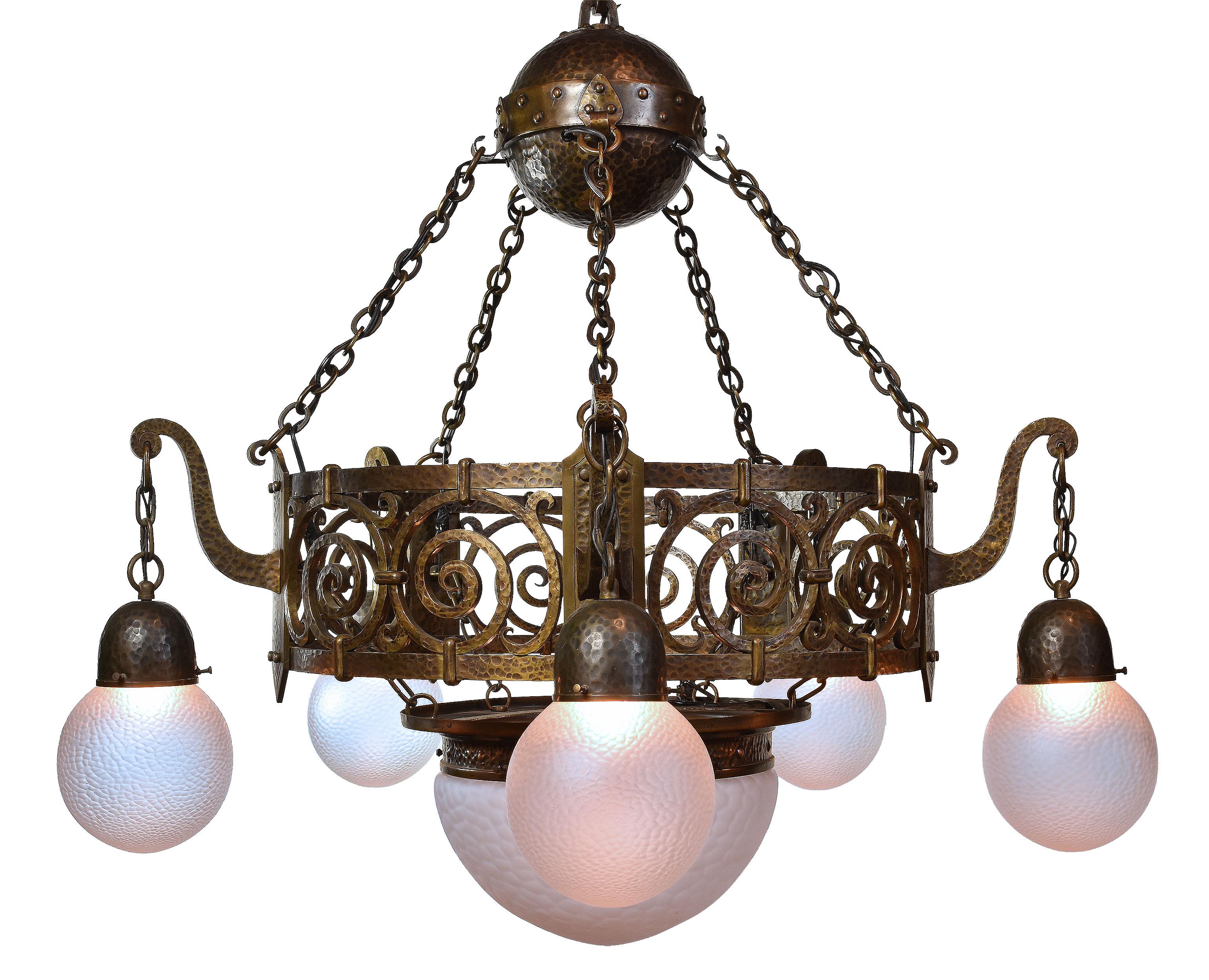 Hammered finishes were iconic of the Arts & Crafts movement which featured a high craftsmanship for everyday objects. This oversized original finish hammered bronze and brass chandelier features five matching hand blown globes that drape around a