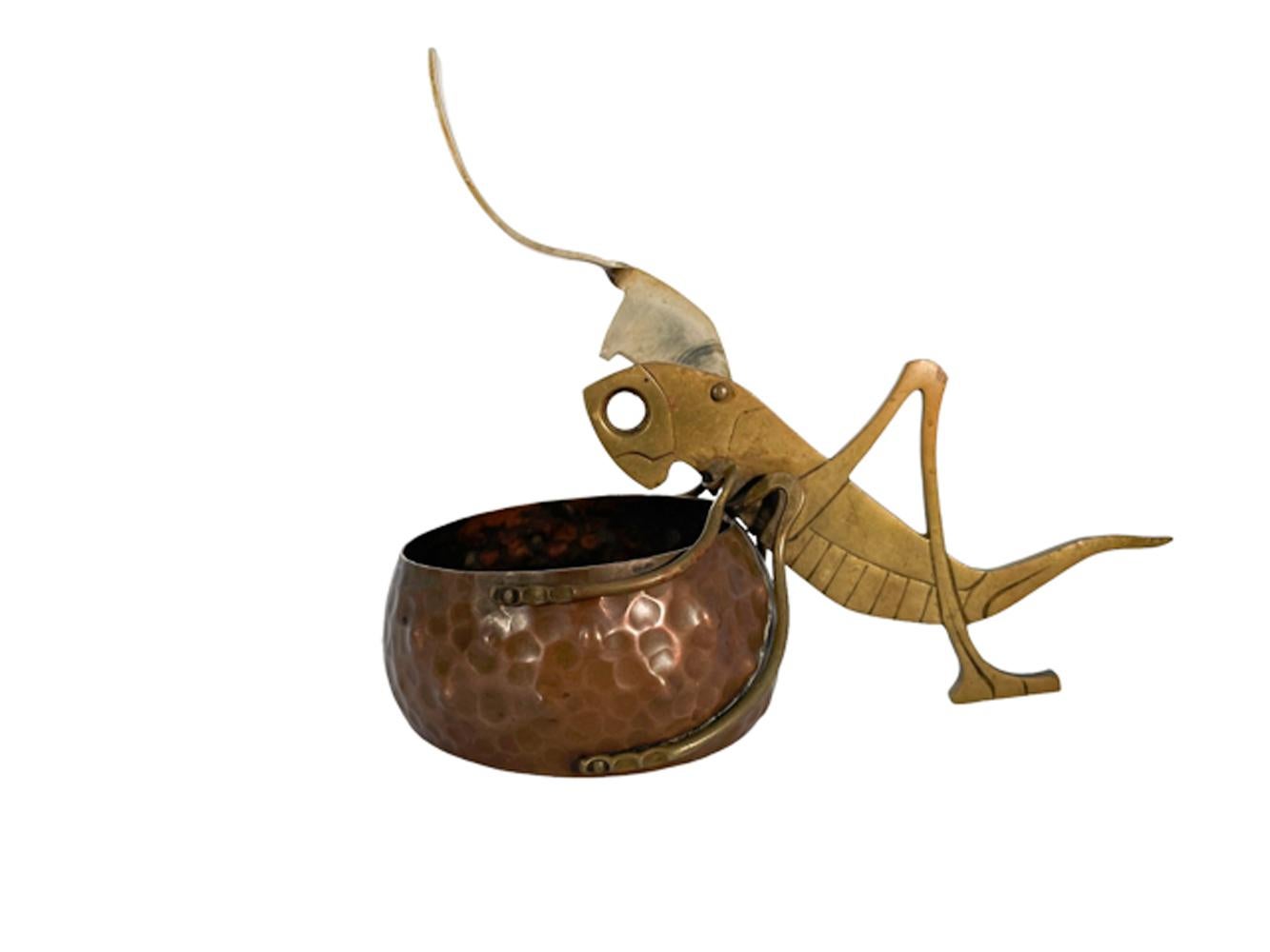 Arts and Crafts cigar cutter / ashtray in the manner of Ignatius Taschner in the form of a cut brass grasshopper with incised detail holding onto a hammered copper pot with its front legs, the grasshopper's steel antennae raise up to cut the cigar