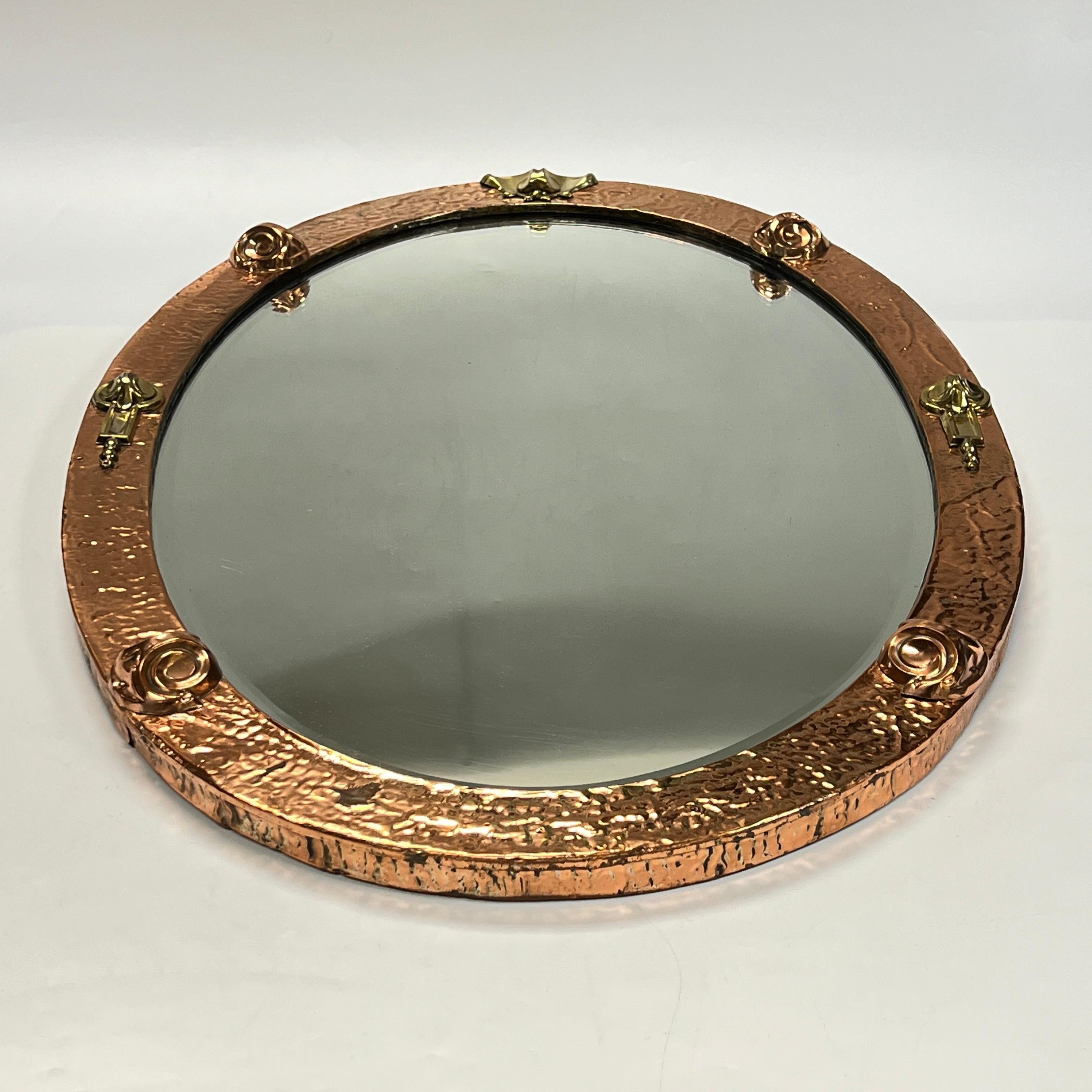 Fine oval-shaped mirror in the Arts and Crafts style, hand-hammered copper over wooden frame with raised, applied brass designs including scrolls and volutes.
