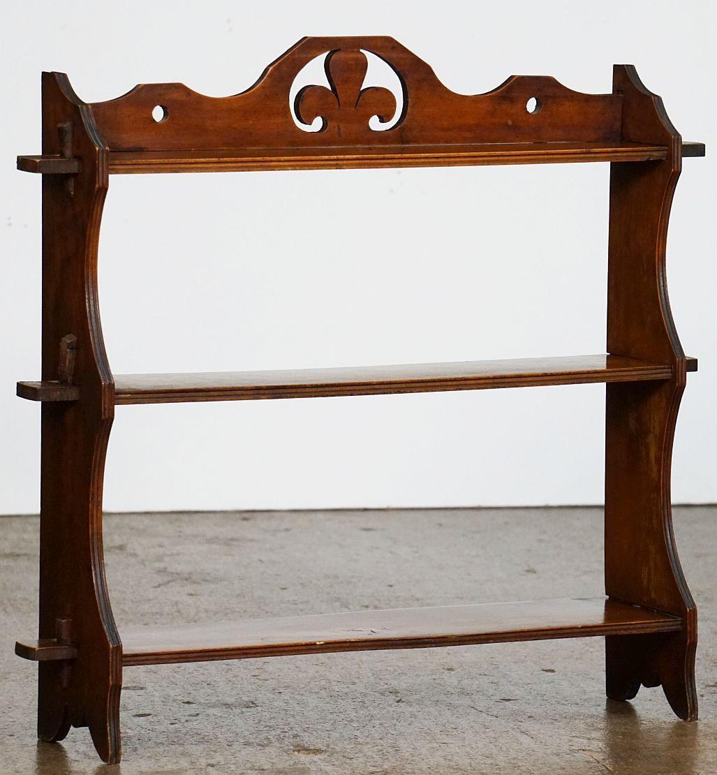 A fine English hanging curio shelf of mahogany, from the Arts and Crafts period, featuring three moulded shelves adjoined by fitted, shaped wood side panels, with decorative gallery backsplash above the top shelf, with a stylized Prince of Wales