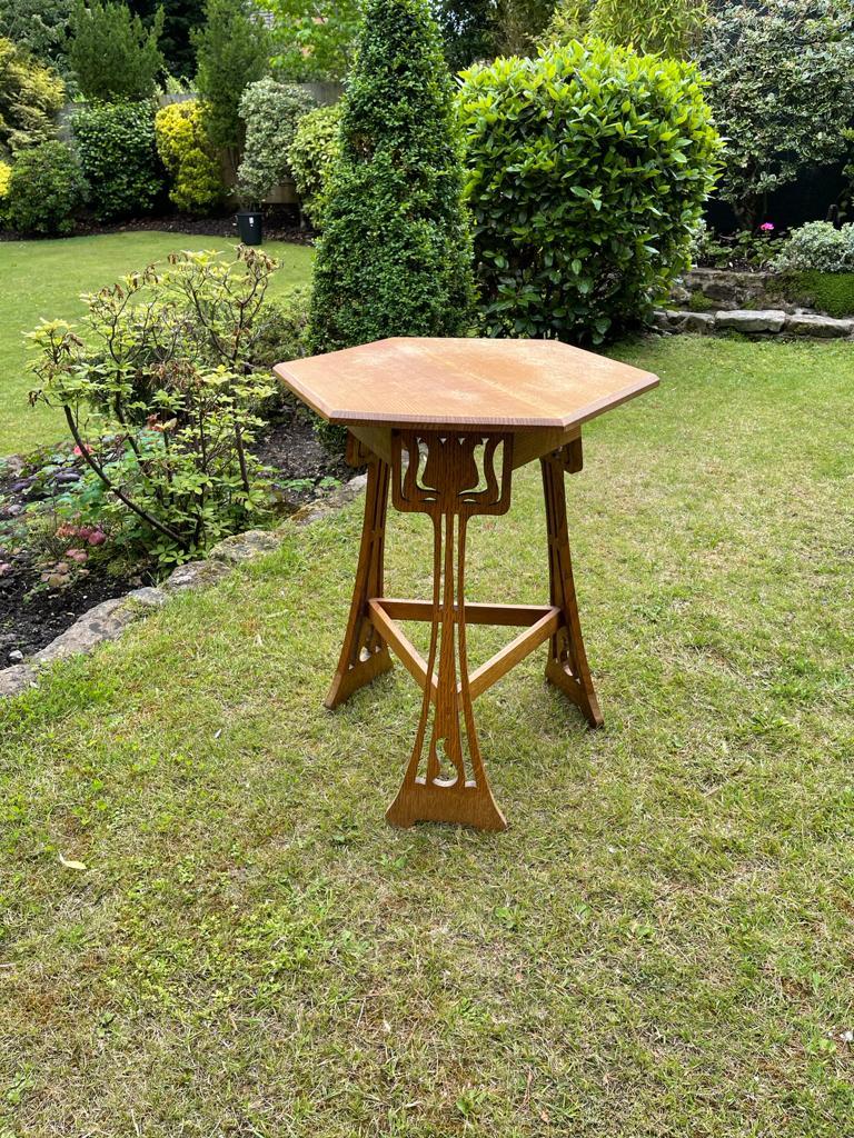 Leonard Wyburd, a liberty and Co 'Sigebert' oak side table with shaped and moulded top and stylised floral cut-outs to the three legs united by three stretchers.