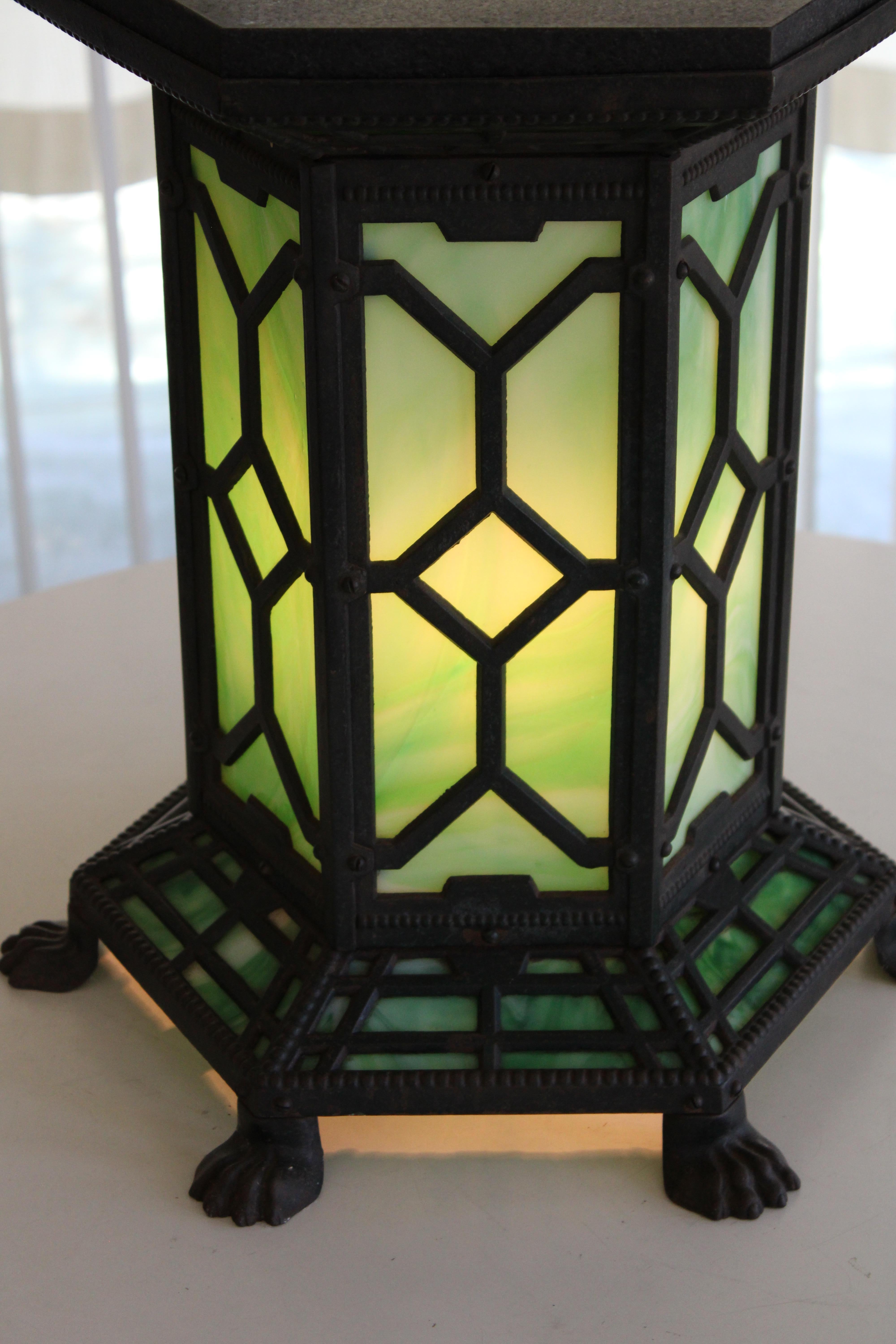 Arts and Crafts lighted table lamp attributed to Bradley & Hubbard.  Old cast iron lighted table, black painted iron and green slag glass, in hexagonal form with black marble top and lion's claw feet. On/off switch at base.  All glass is original
