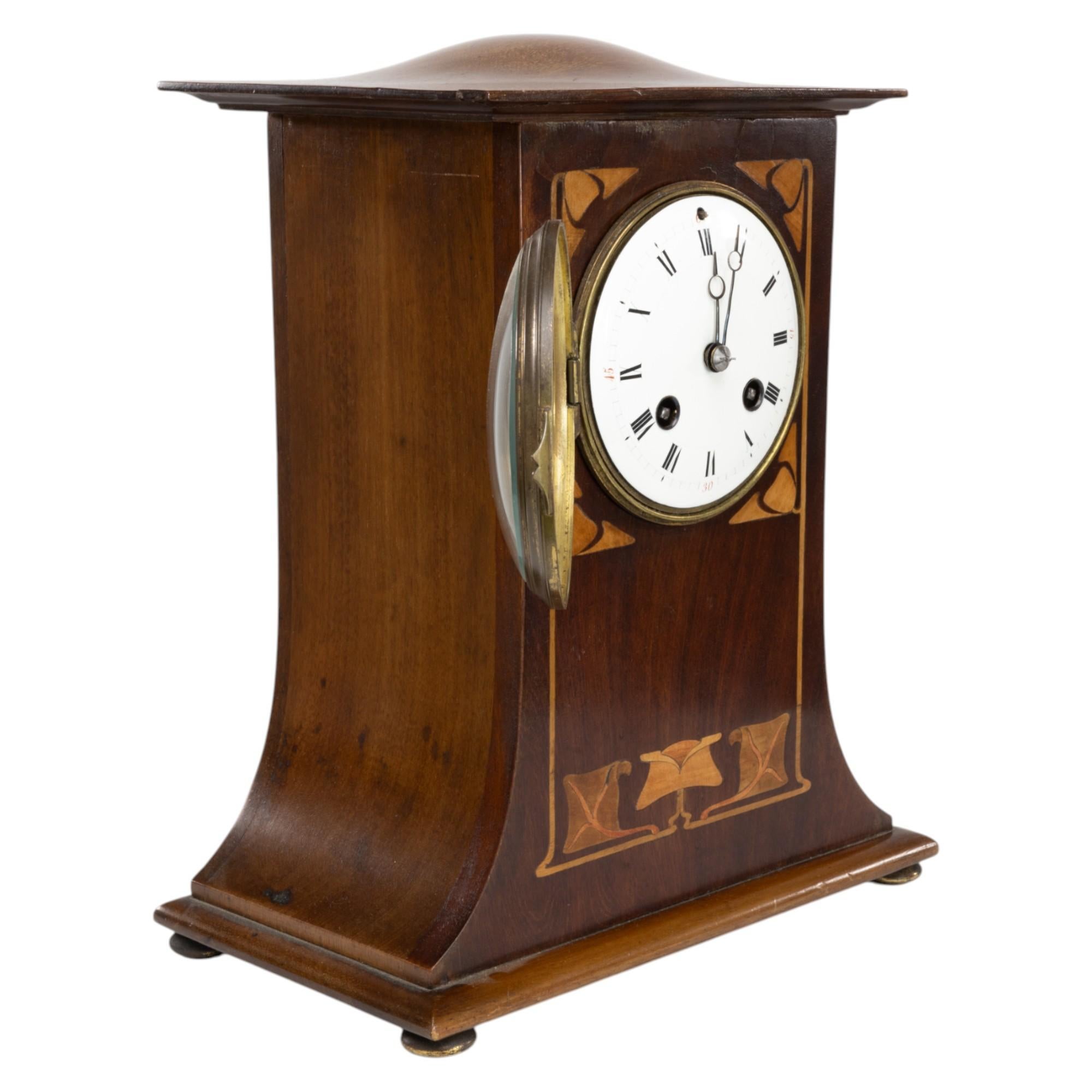 Liberty & Co., London. An Arts and Crafts mahogany mantle clock with stylised floral inlay to the front panel. The case has a gently domed top and sweeping architectural form, design elements that strongly recall the influence of C. F. A.