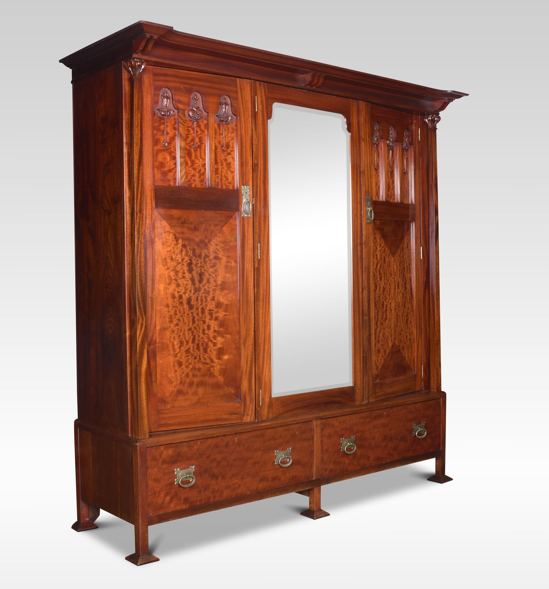 Arts & Crafts mahogany wardrobe, the flared cornice pediment above pilaster columns, to the large central beveled mirrored door flanked by two-panel doors having acanthus seed pod detail. Opening to reveal maple interior and large hanging area. To