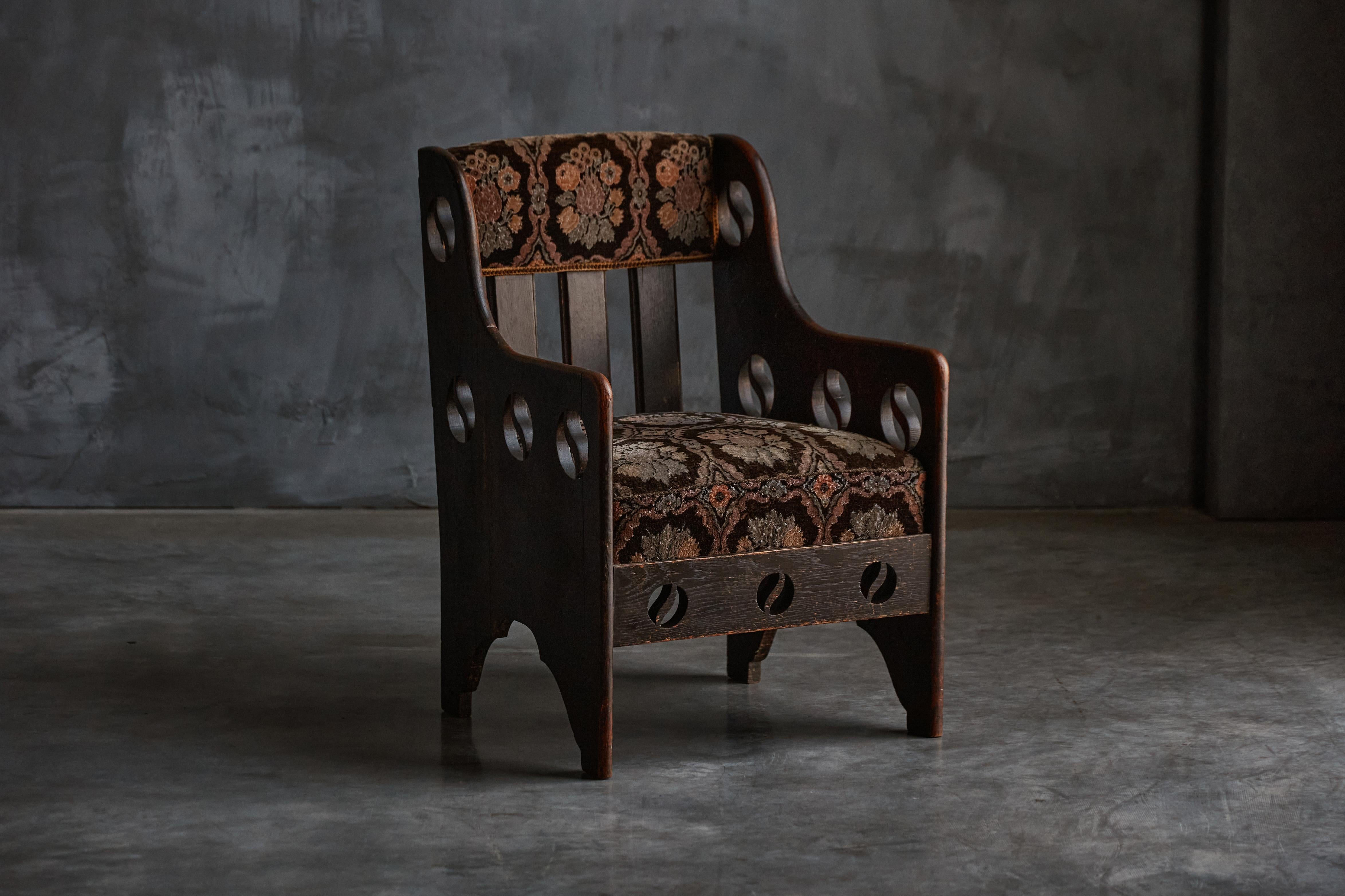 Stunning c.1900 Arts and Crafts oak lounge chair retailed by Goodyers of Regent Street, known for their association with Liberty & Co. The armchair features intricate yin and yang cut-out motifs and a classic drop-in seat. Its original needlepoint