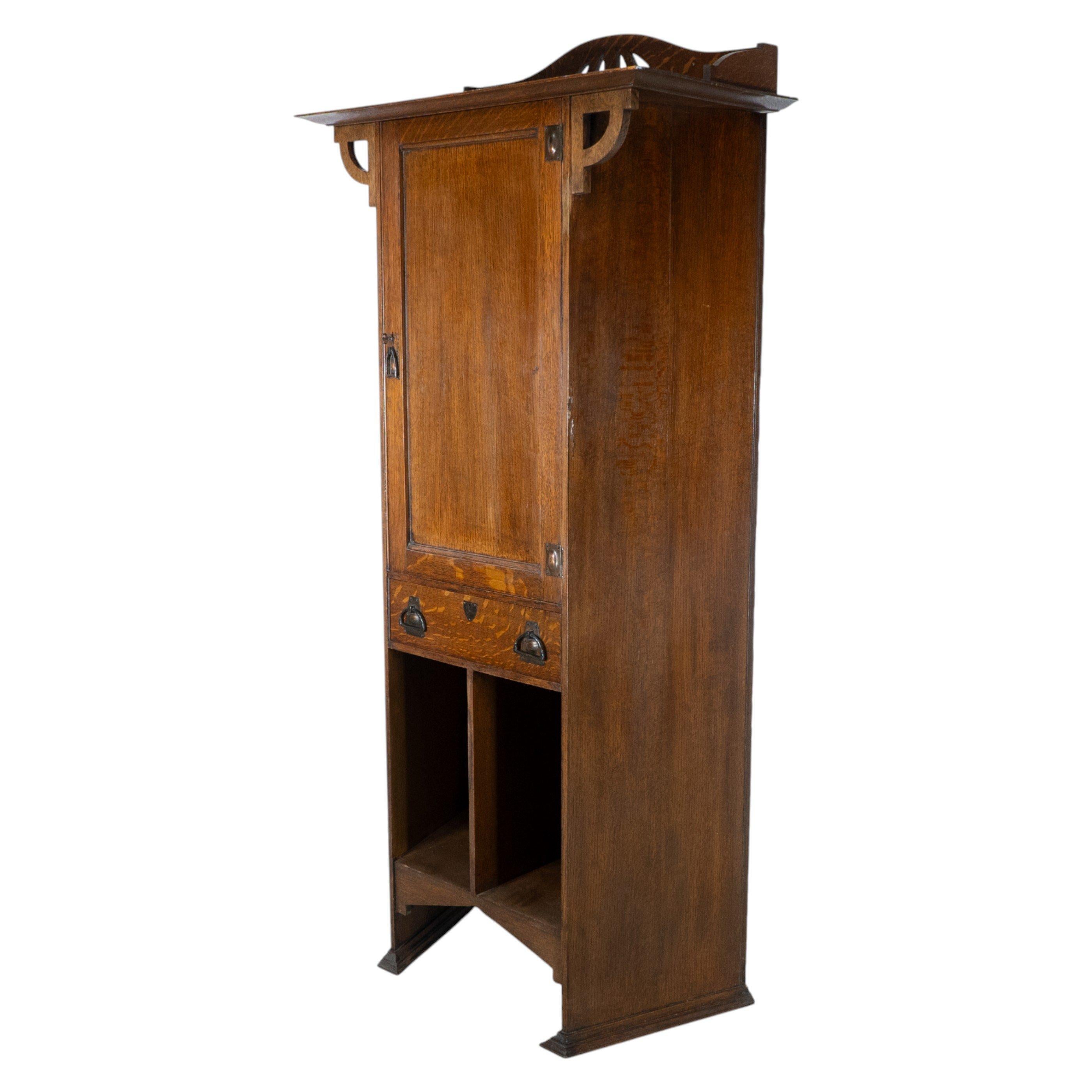 Shapland & Petter. Ein eckiger Schrank aus Eichenholz im Arts and Crafts-Stil mit einem geformten und mit Laubsägearbeiten versehenen Giebel und einem von geschwungenen Klammern getragenen Oberteil. Der obere Schrank hat Kupferscharniere und einen
