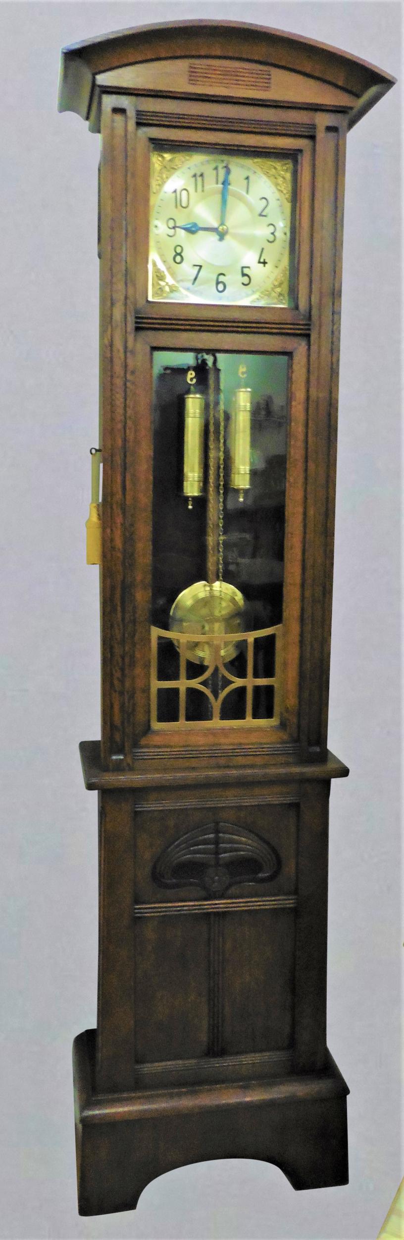 Fine Arts and Crafts oak cased Longcase clock standing on a raised plinth with beautifully decorated panel below the glazed door with raised brass decoration. 

 Curved pediment above the silvered dial with brass corner spandrels and silvered