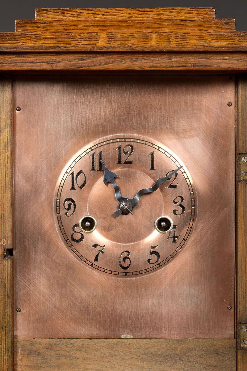Arts and Crafts oak cased mantel clock. Two columns with brass capitals support either side of the dial with brass inlay decoration to the front panel.
 
Copper dial with Arabic numerals and original ‘blued’ steel hands.
 
Eight day German