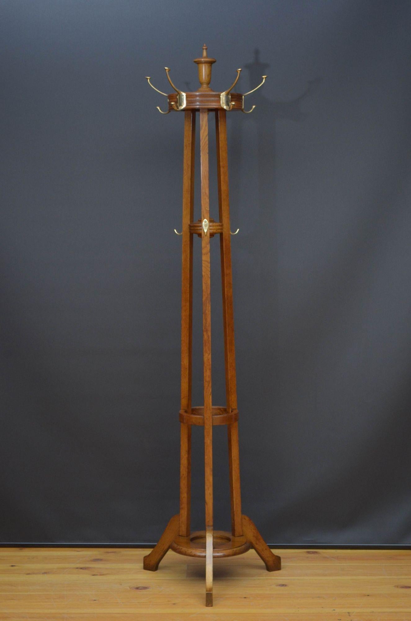 R023 Arts and Crafts oak hat stand, having brass hooks on revolving platform with finial to the top on 3 solid oak supports with further 3 brass hooks terminating in shaped legs and united by circular base with reeded edge. This antique coat stand