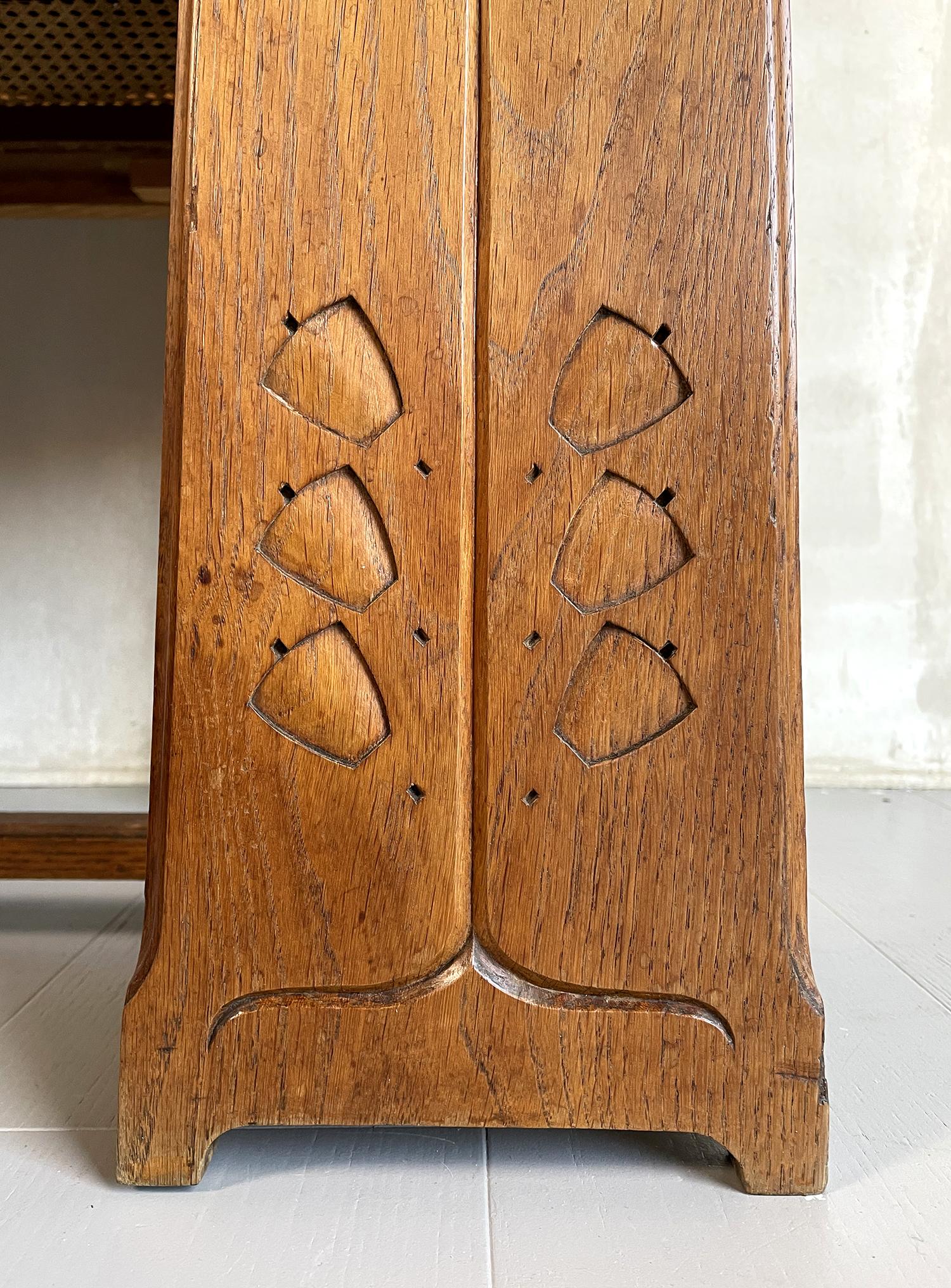 Flurschrank aus blonder Eiche im Arts-and-Crafts-Stil, 1900. Die Pfosten der Rohrbank sind mit stilisierten Glockenblumen verziert, der große, abgeschrägte Spiegel ist von fünf patinierten Messinghaken umgeben. Um Ihre Regenschirme und Ihre Stöcke