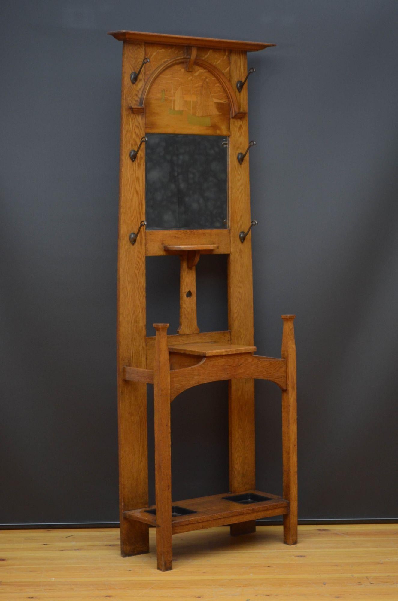Sn5432 Arts and crafts coat stand in oak, having moulded top above ship inlaid panel, original bevelled edge mirror and a shelf flanked by six original hooks the base having small storage compartment, all standing on square legs united by undertier