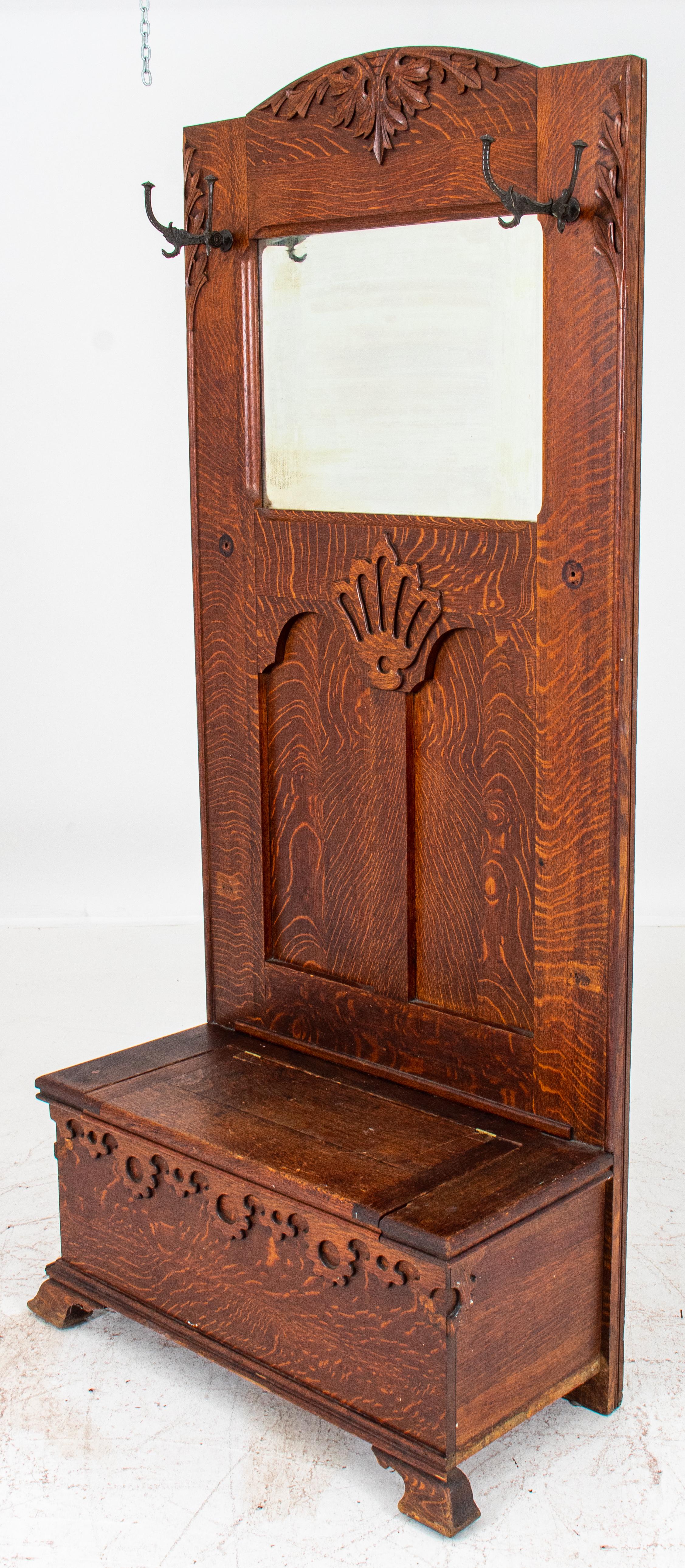 Arts and crafts oak hall stand, ca. 1910, and with 
A stylized foliate crest rail and sides with hooks for coats centering a mirror, above an hinged lidded bench for storage. Measures: 80