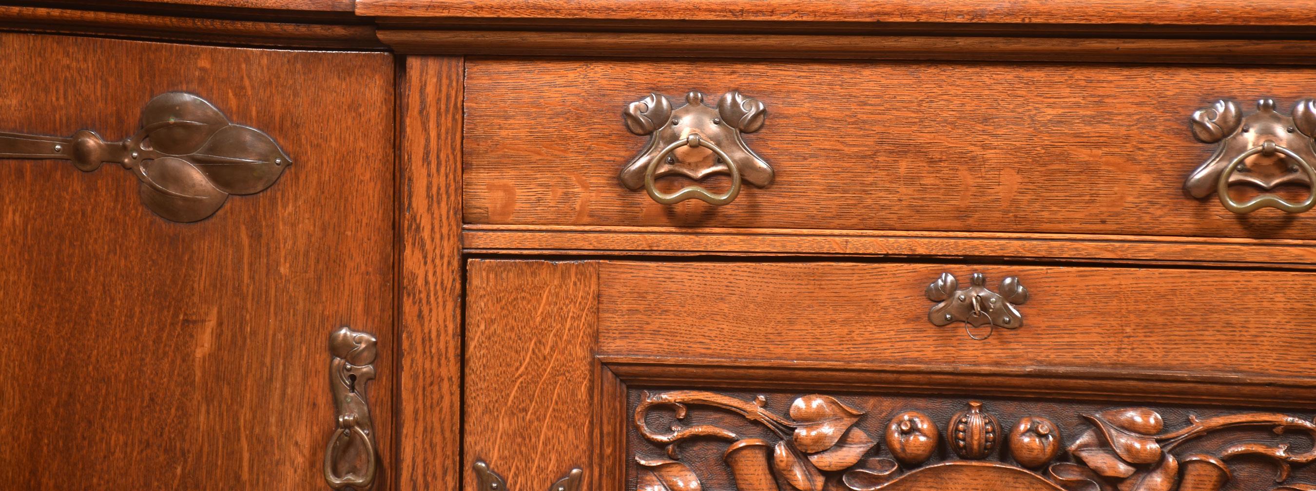 Late 19th-century oak sideboard in the Arts & Crafts style, the large rectangular top with bowed front to the large freeze drawer with stylised handles. Above three cupboard doors, one door opening to a lead-lined cellarette drawer, the body of the