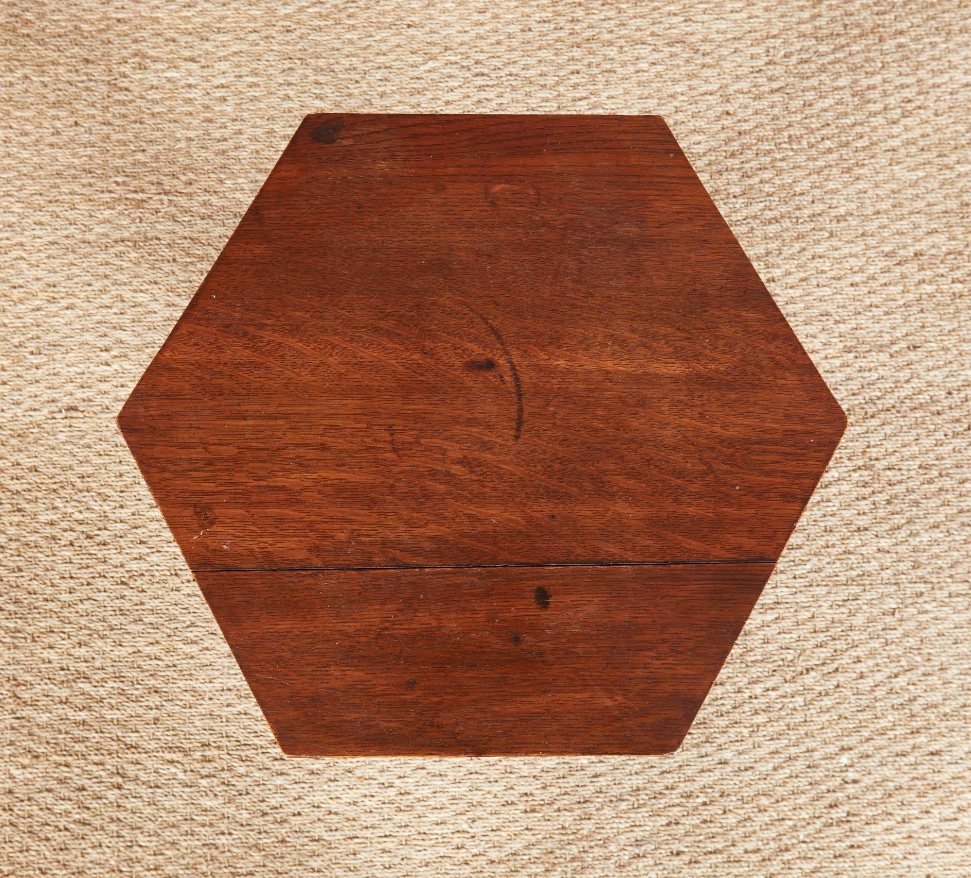Table Arts and Crafts en chêne scié sur quartier, avec un plateau hexagonal et une tablette inférieure en forme, reposant sur trois pieds plats et effilés se terminant par des pieds arqués et décorés de motifs trilobés. Une forme attrayante et utile