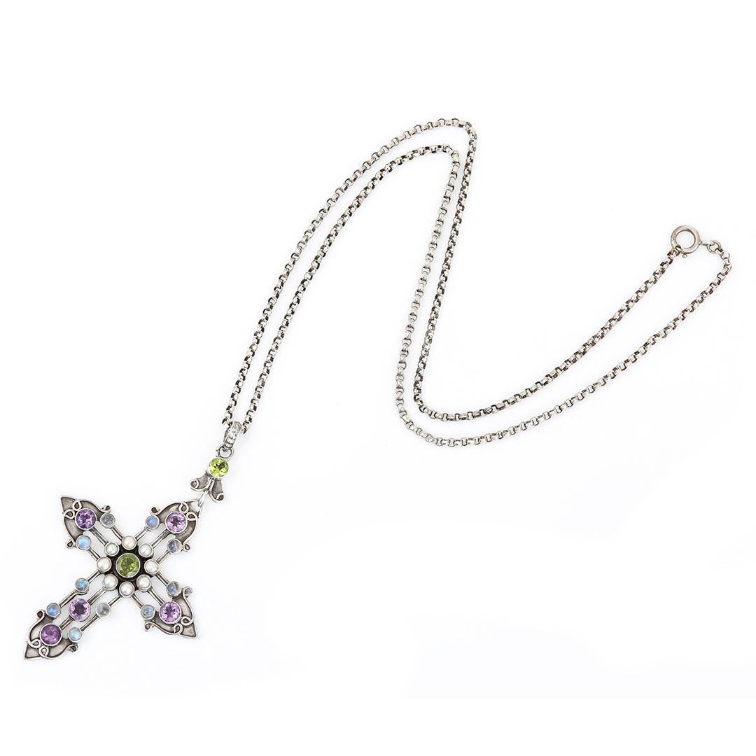 A beautiful Arts and Crafts sterling silver gem set brooch to include amethyst, peridot, moonstone and pearl. Dating from circa 1900 the cross of crucifix form has a centra peridot and pearl cluster from which the four points of the cross emanate.