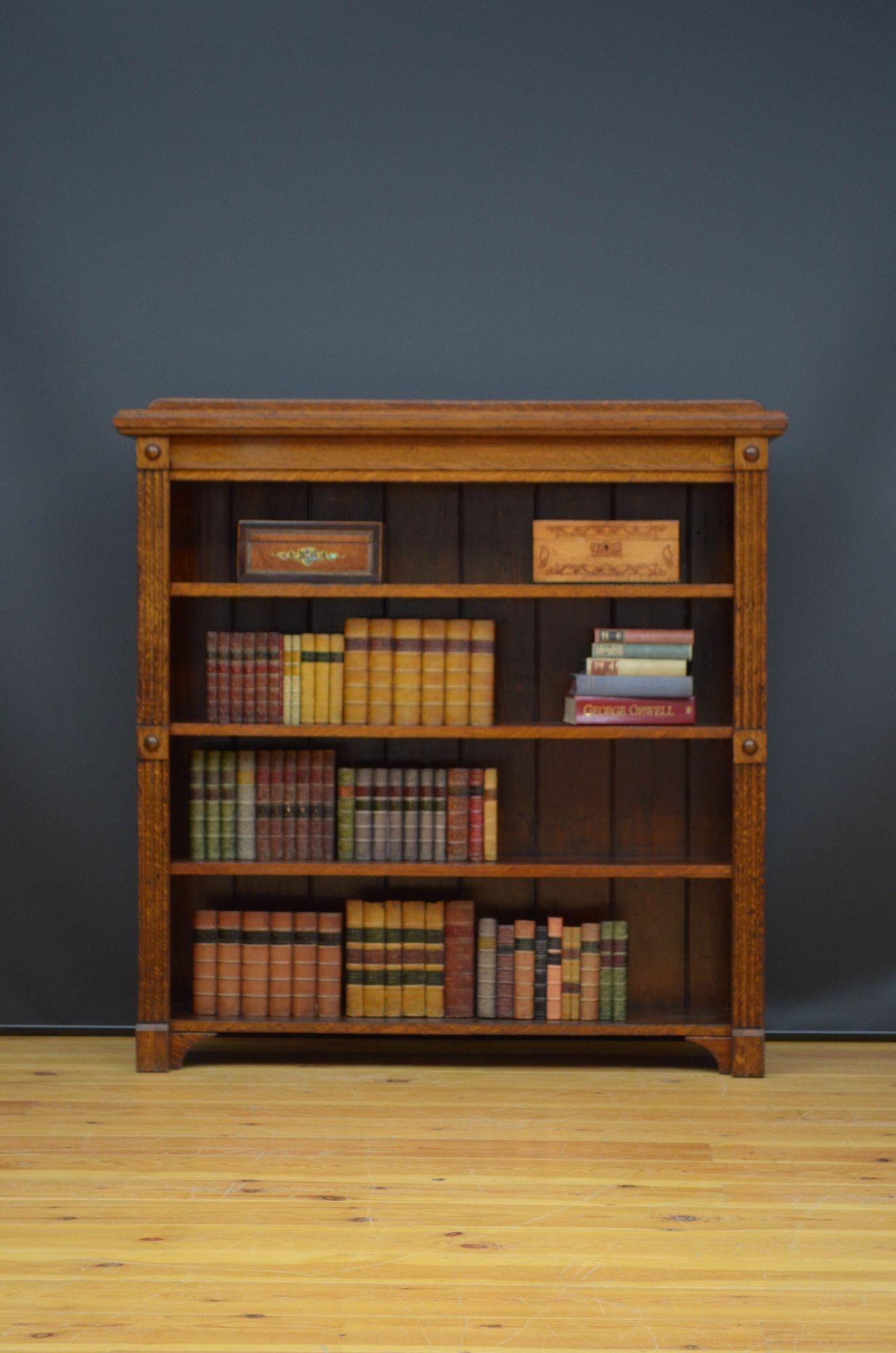 Sn5382 Arts and Crafts open bookcase in solid oak, having shaped upstand to the back, moulded top and three height adjustable shelves flanked by reeded pilasters and carved roundels, all standing on shaped plinth base. This antique bookcase retains