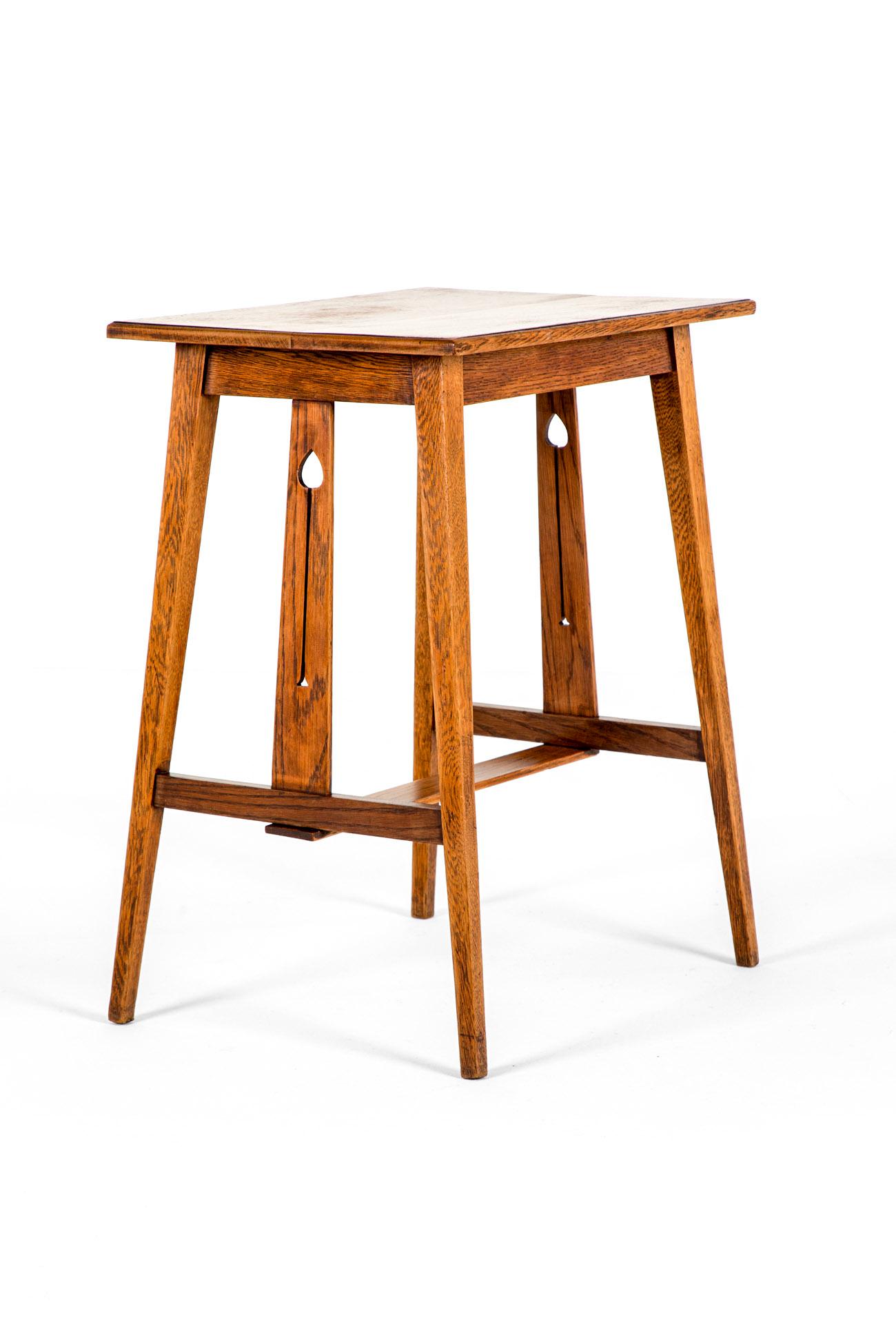 Table d'appoint en chêne clair de la période Arts and Crafts, avec un plateau carré soutenu par des supports percés à chaque extrémité.

Quatre pieds légèrement effilés réunis par un châssis en forme de 