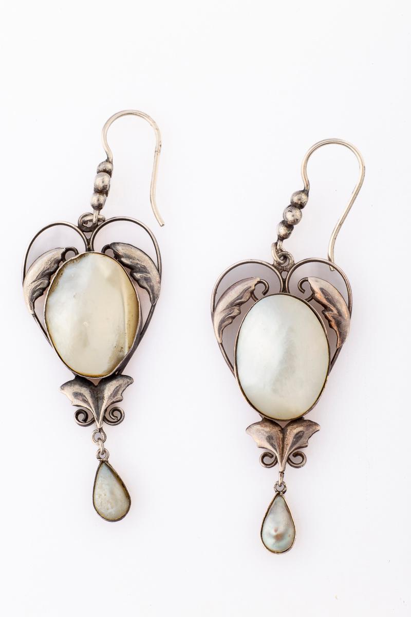 A dramatic size makes these exceptional, hand made, Arts and Crafts earrings atypical. The center is shaped like a heart that delicately frames the oval mother of pearl. Ah the mother of pearl, it has rainbow hues as it moves. Small graceful leaves