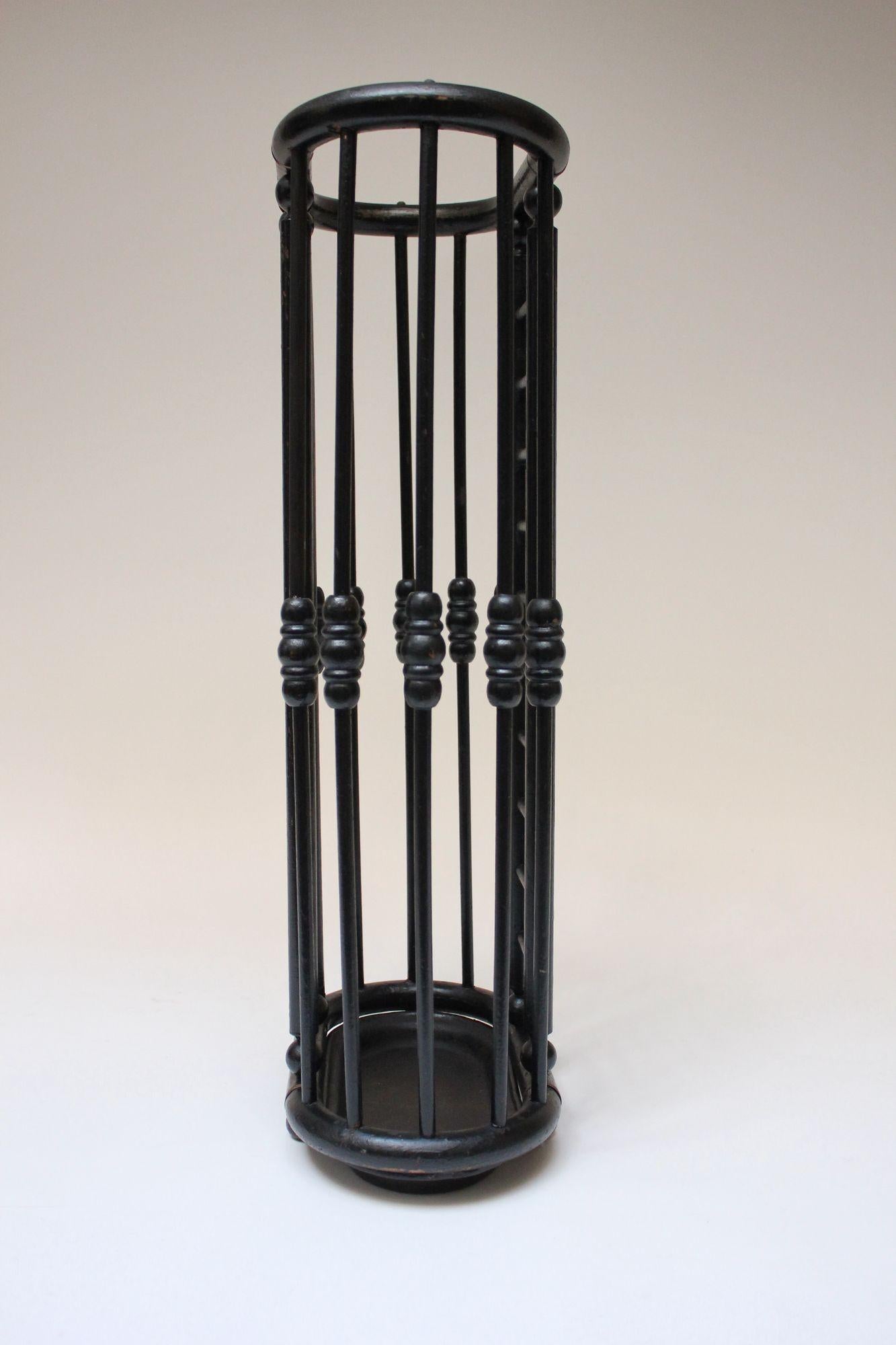 Umbrella stand composed of an ebonized-oak stick and ball constructed frame with painted black cast iron base and brass hardware (ca. late 19th Century/early 20th Century USA).
Some of the spindles are slightly bowed on one side, and there is light