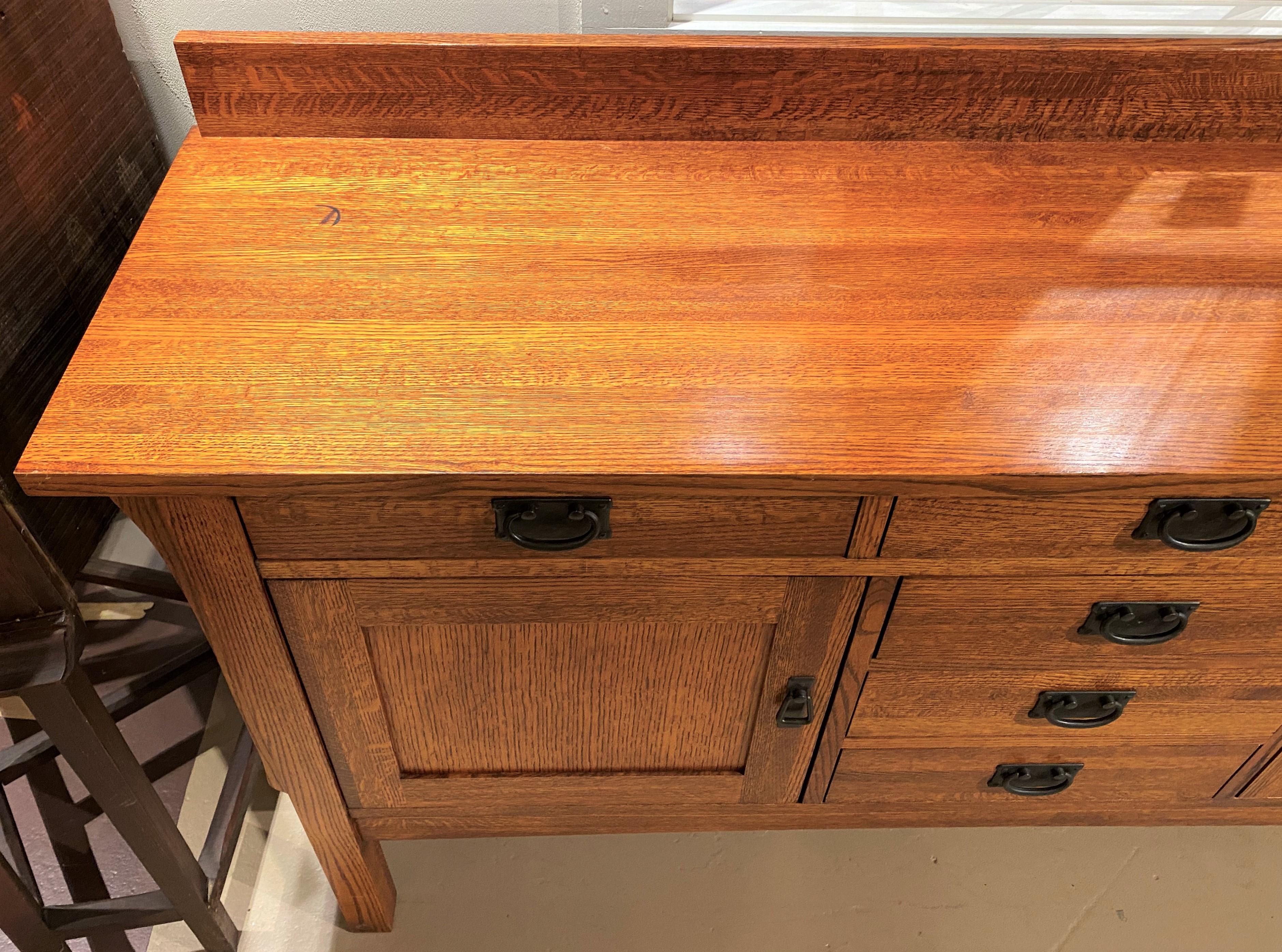 A fine mission style quarter sawn oak sideboard by Michaels Company, Sacramento, CA, with a rectangular top and backsplash surmounting three fitted frieze drawers over three center fitted dovetailed drawers, flanked by two paneled doors, opening to