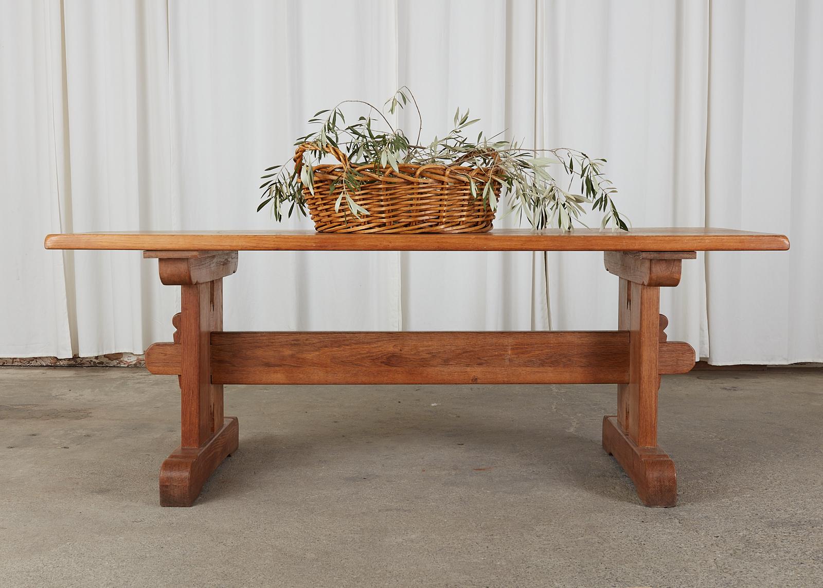 Rustic French oak farmhouse trestle dining table featuring an arts and crafts or craftsman style. The thick 1.5 inch solid top is supported by double pedestal legs conjoined with exposed mortise and tenon joinery. The legs end with simple shoe feet.