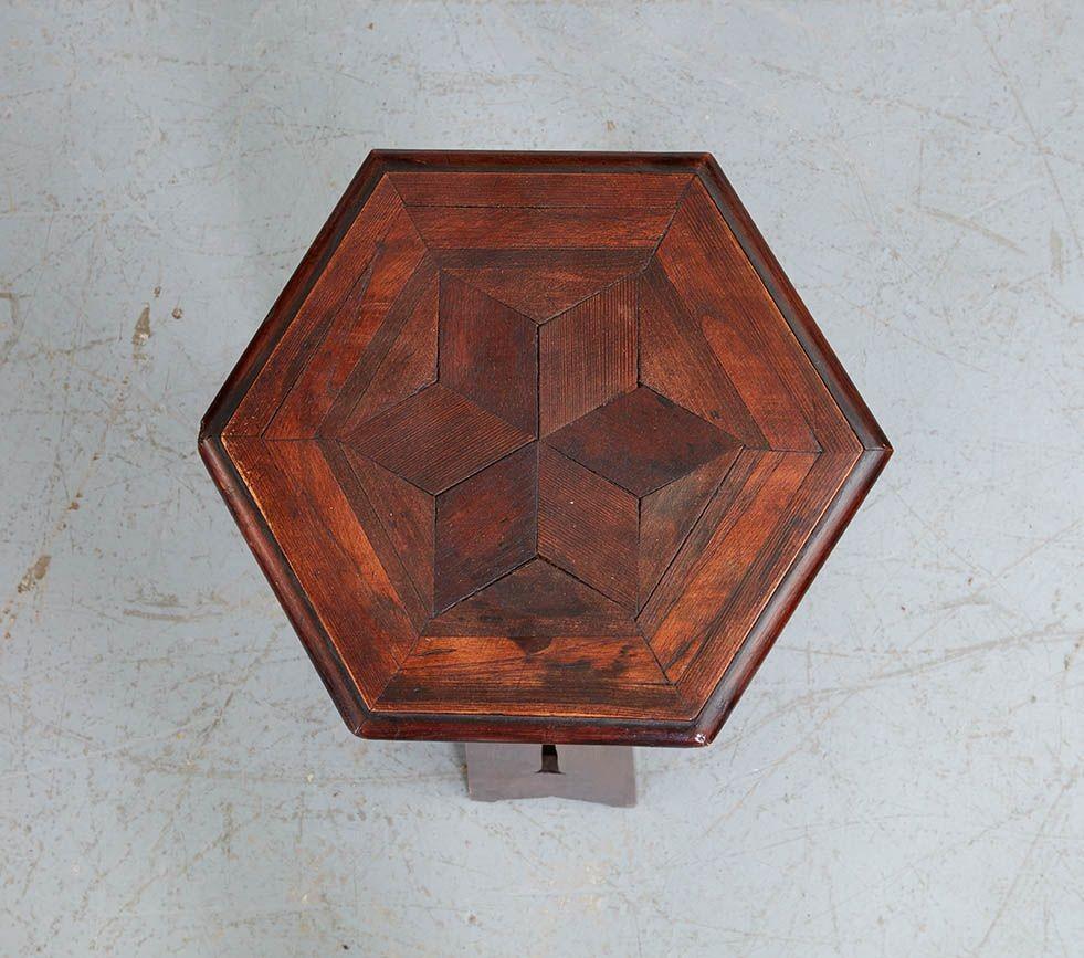 An Arts and Crafts oak tripod table/stand having hexagonal top with geometric border and star inlays over three splayed legs incorporating long stemmed tulip cutouts and shaped feet, joined by a lower stretcher.
