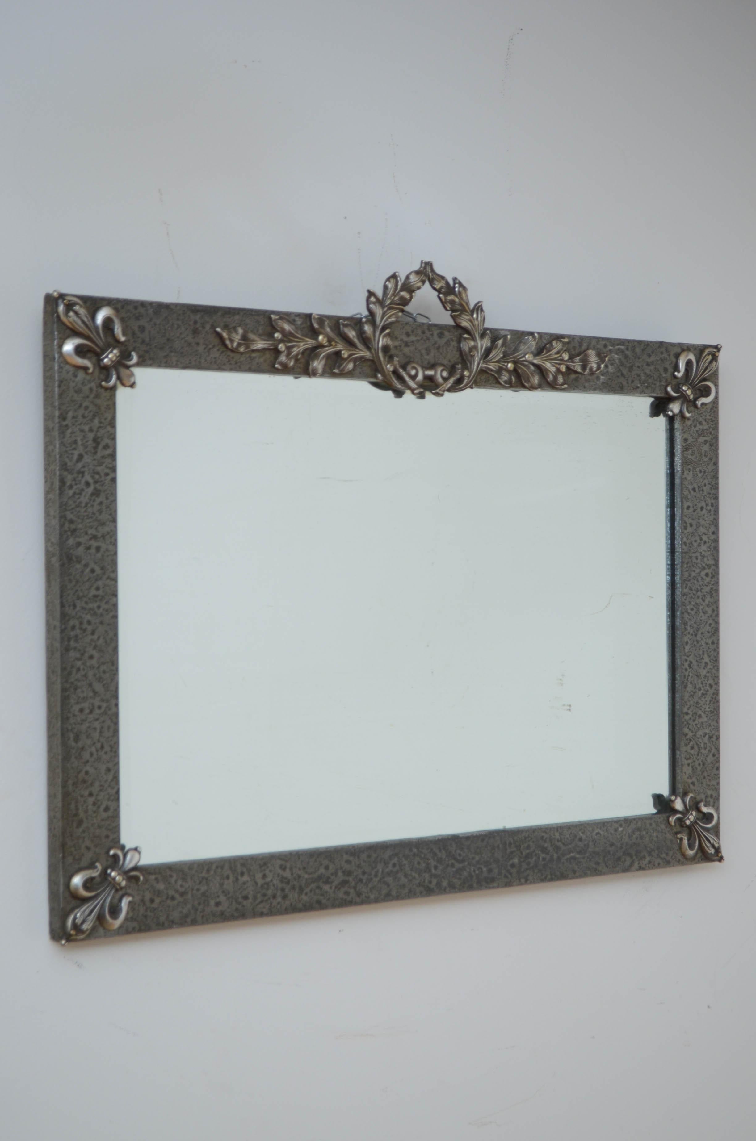 K0552 Stylish Arts and Crafts mirror with original bevelled edge glass in metal hammered frame with fleur de lys decoration to the corners and laurel wreath to the centre. All fitted with original metal back and adjustable hanging chain.
