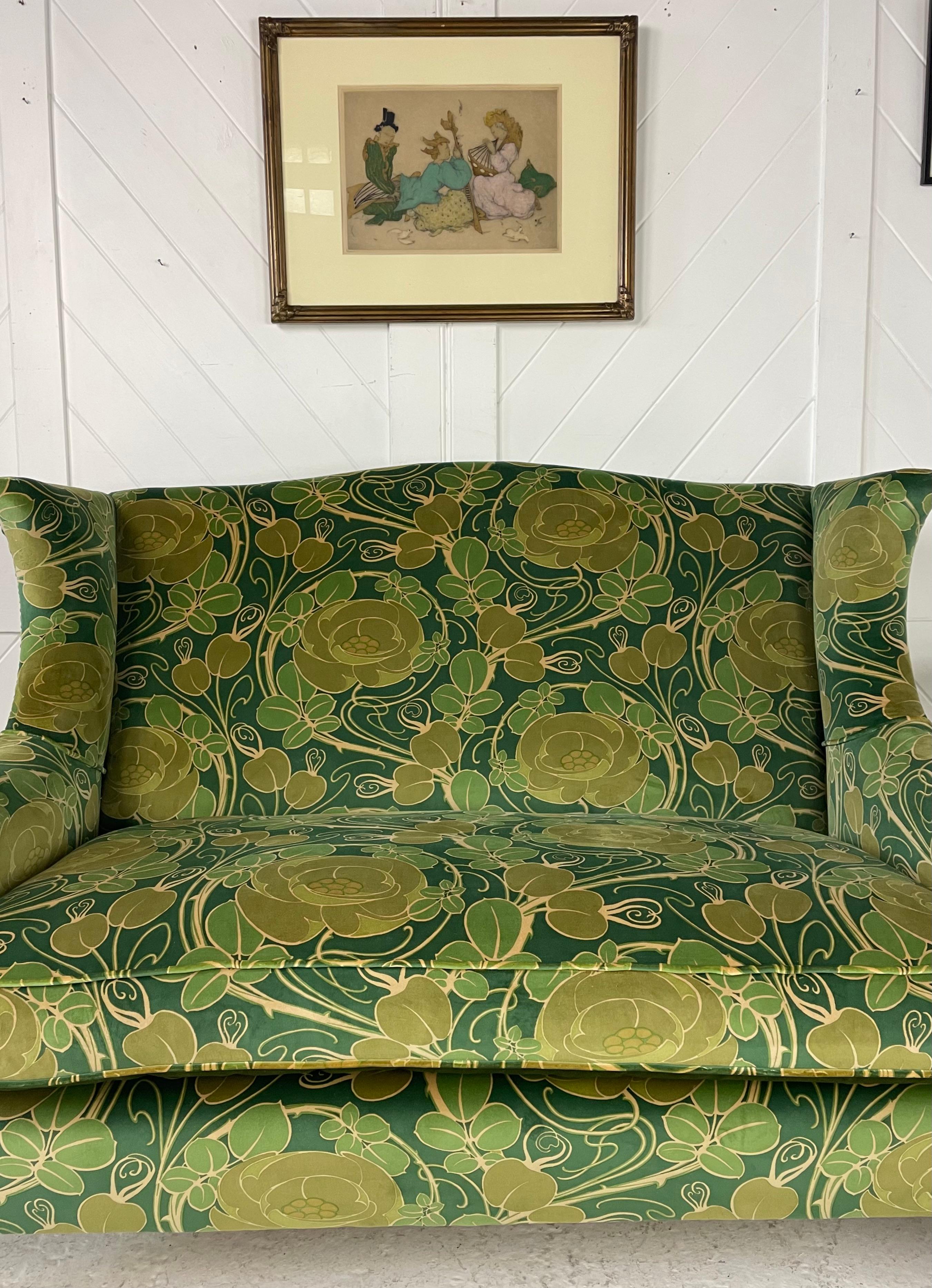 Beautiful Arts and Crafts wingback settee. Probably retailed through Liberty & Co London. Solid beech frame with typical Arts and Crafts oak tapering feet. Traditionally reupholstered and recovered in 'Glasgow Rose' cotton velvet fabric by Patch