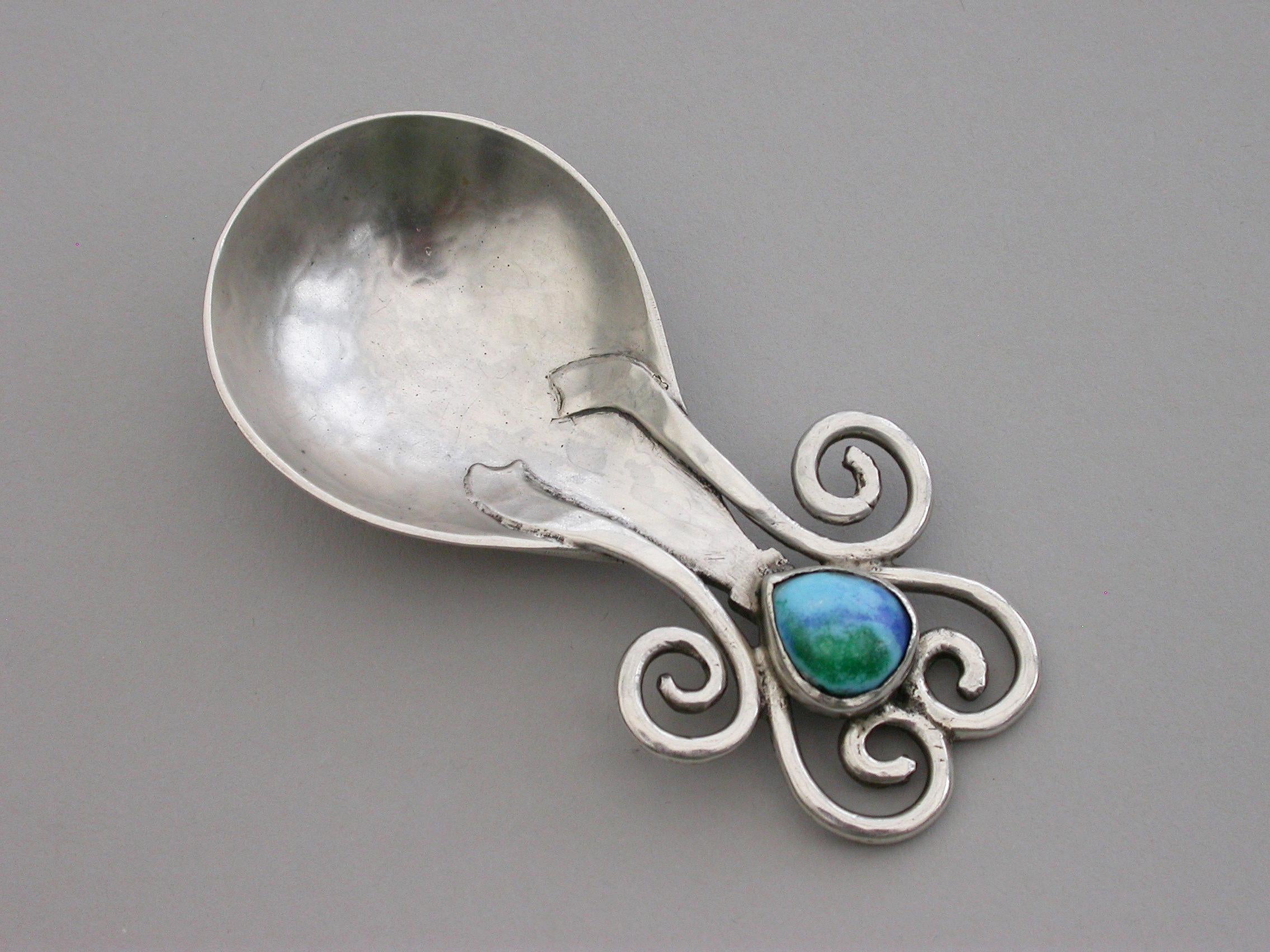 A fine quality rare Arts & Crafts cast silver Caddy spoon with hammered fig shaped bowl, the handle set with turquoise blue and green enamel boss between four coiled and linked wires.

By Ramsden & Carr, London, 1909.