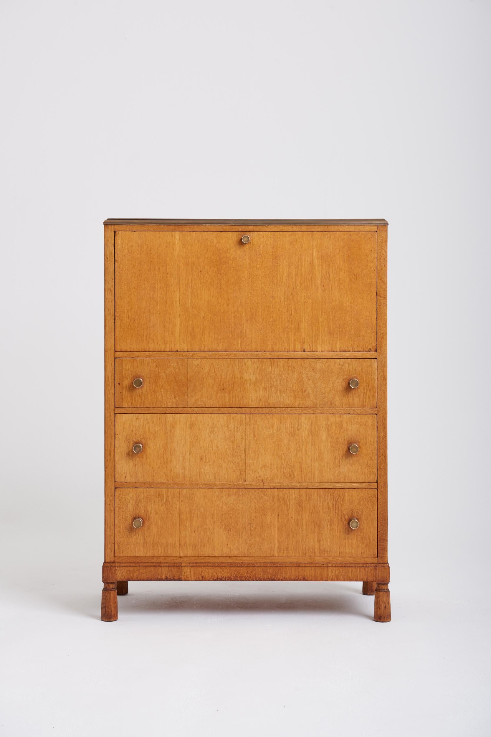 An Arts & Craft oak secretaire, by H Morris & Co of Glasgow, with a most unusual Bakelite top with a brass mount, supported on faceted tapered solid oak feet, the three drawers with brass faceted knobs below an abbattant revealing an oak lined