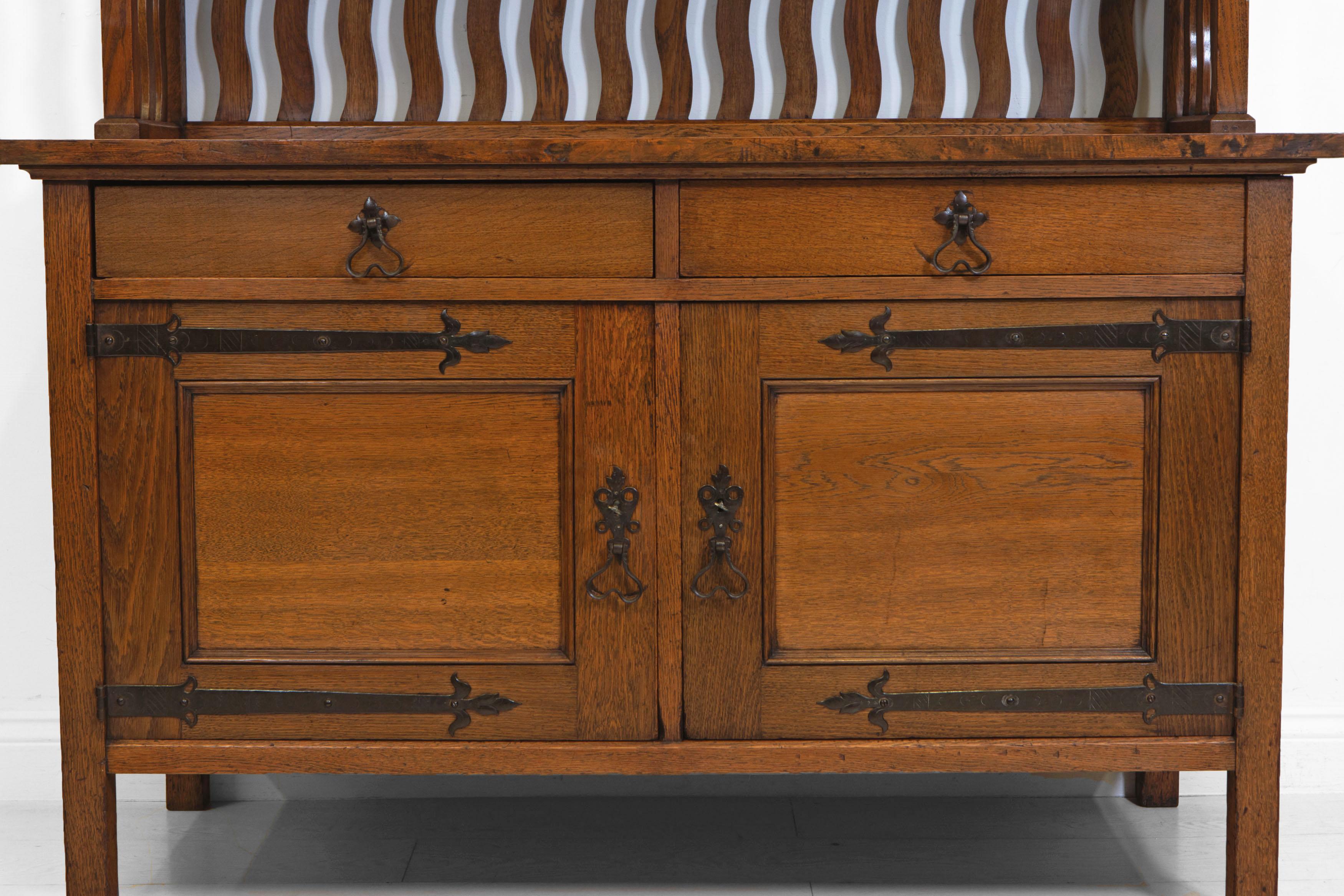 Arts & Crafts oak sideboard cabinet in the Liberty & Co manner, with decorative metal strap work hinges and handles, and a wavy slatted back gallery. English. Circa 1900.

In excellent clean condition, it has has been sympathetically re-finished,