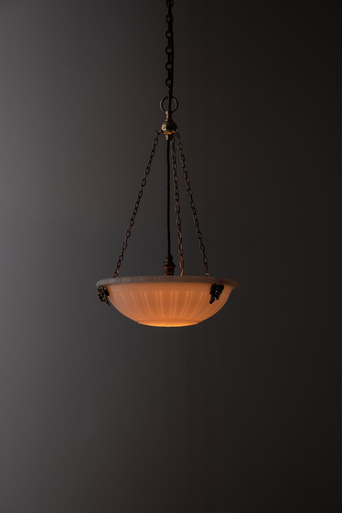

A Large pressed glass moonstone plafonnier pendant light. c.1920

Heavy duty pressed milk glass of fluted design with lotus flower, supported by decorative rams head integral hooks, ball hook and ceiling plate. Chains could be shortened to suit