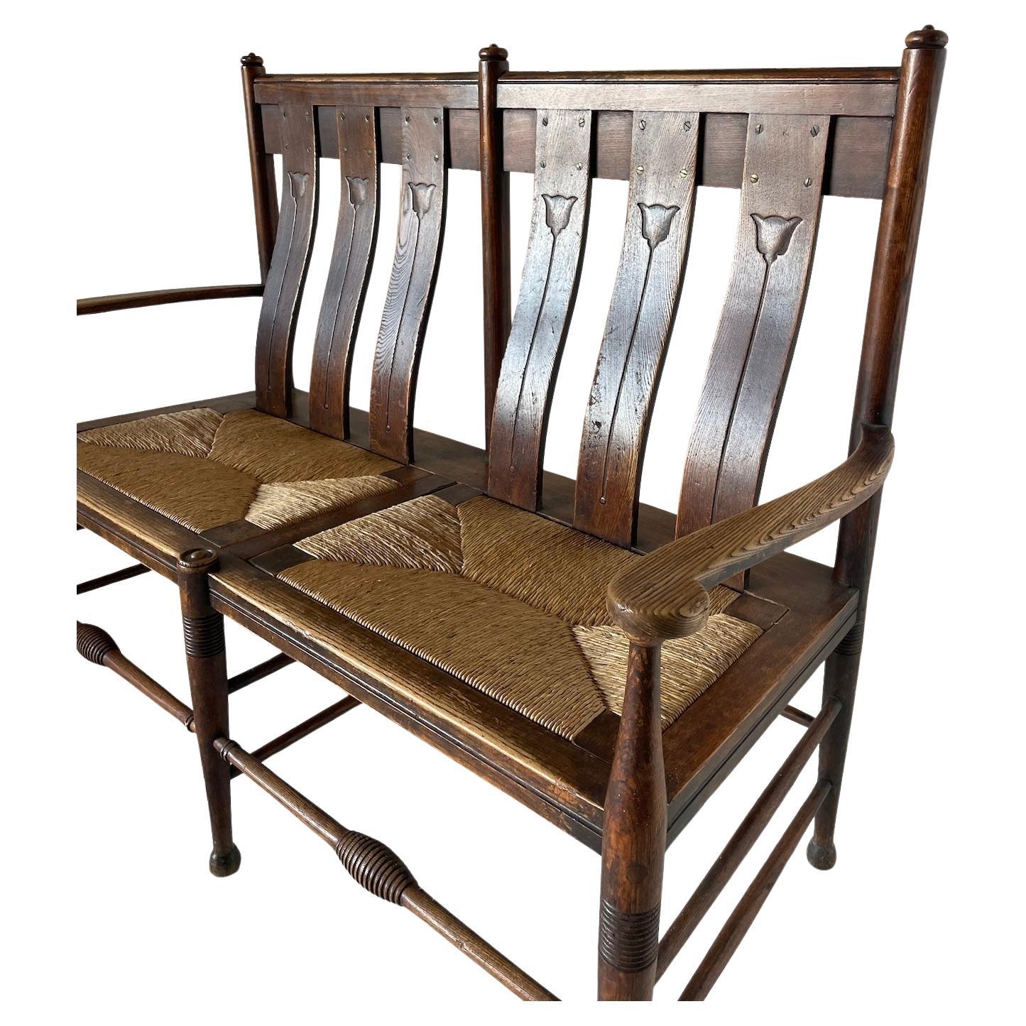 Sedia a 2 posti con cornice in rovere Arts & Crafts

Schienale ergonomico con decorazione a tulipano stilizzato

Gambe tornite e sedili in giunco

Da William Birch di High Wycombe

Circa 1900

Altezza 109 cm. Larghezza 136 cm. Profondità 58 cm.