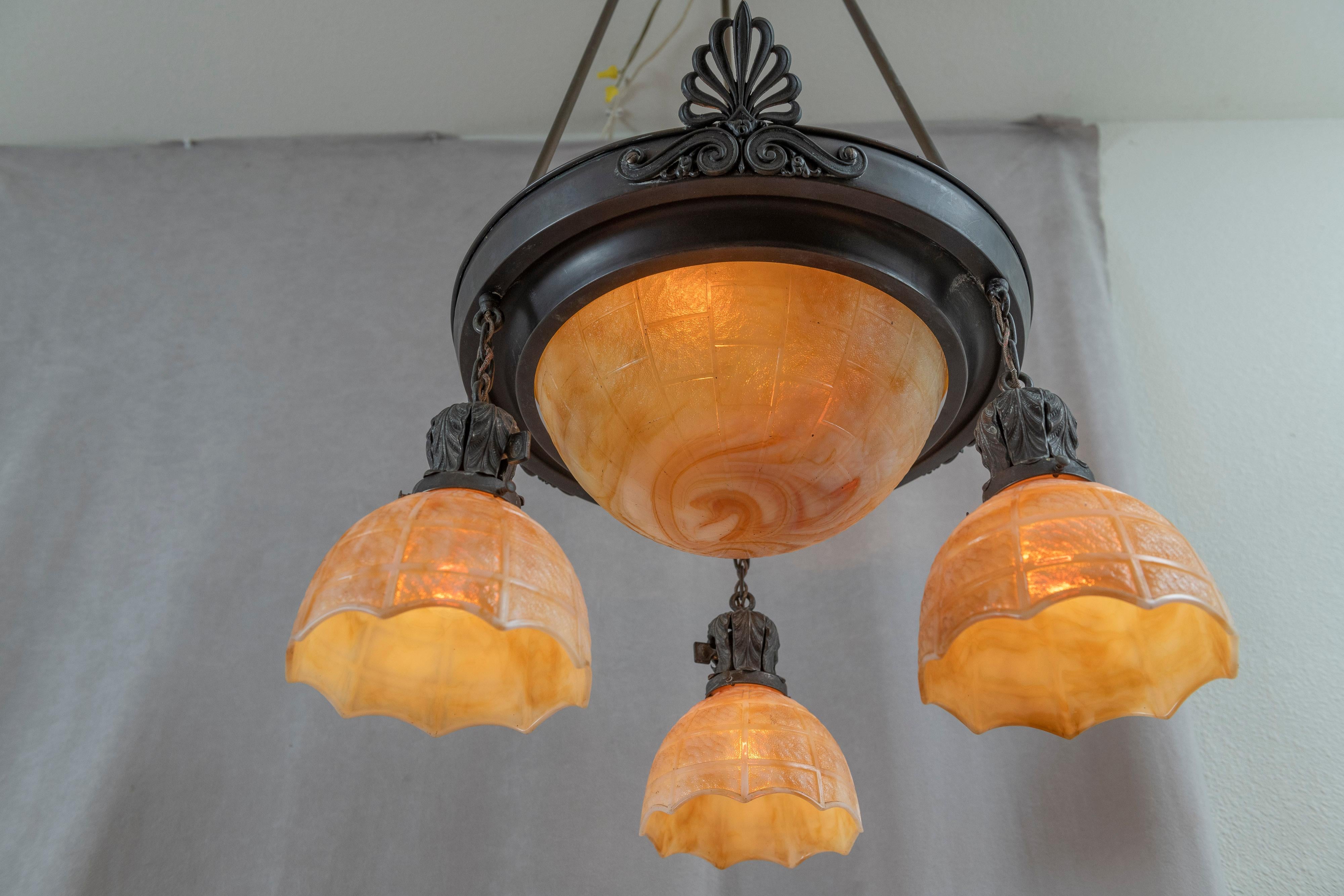 This handsome chandelier is simple and elegant. The richly patinated metalwork supports and inverted dome which is surrounded by 3 matching glass shades. We know the glass to be made by Kokomo Glass. The glass is thick and opaque so lightbulbs are