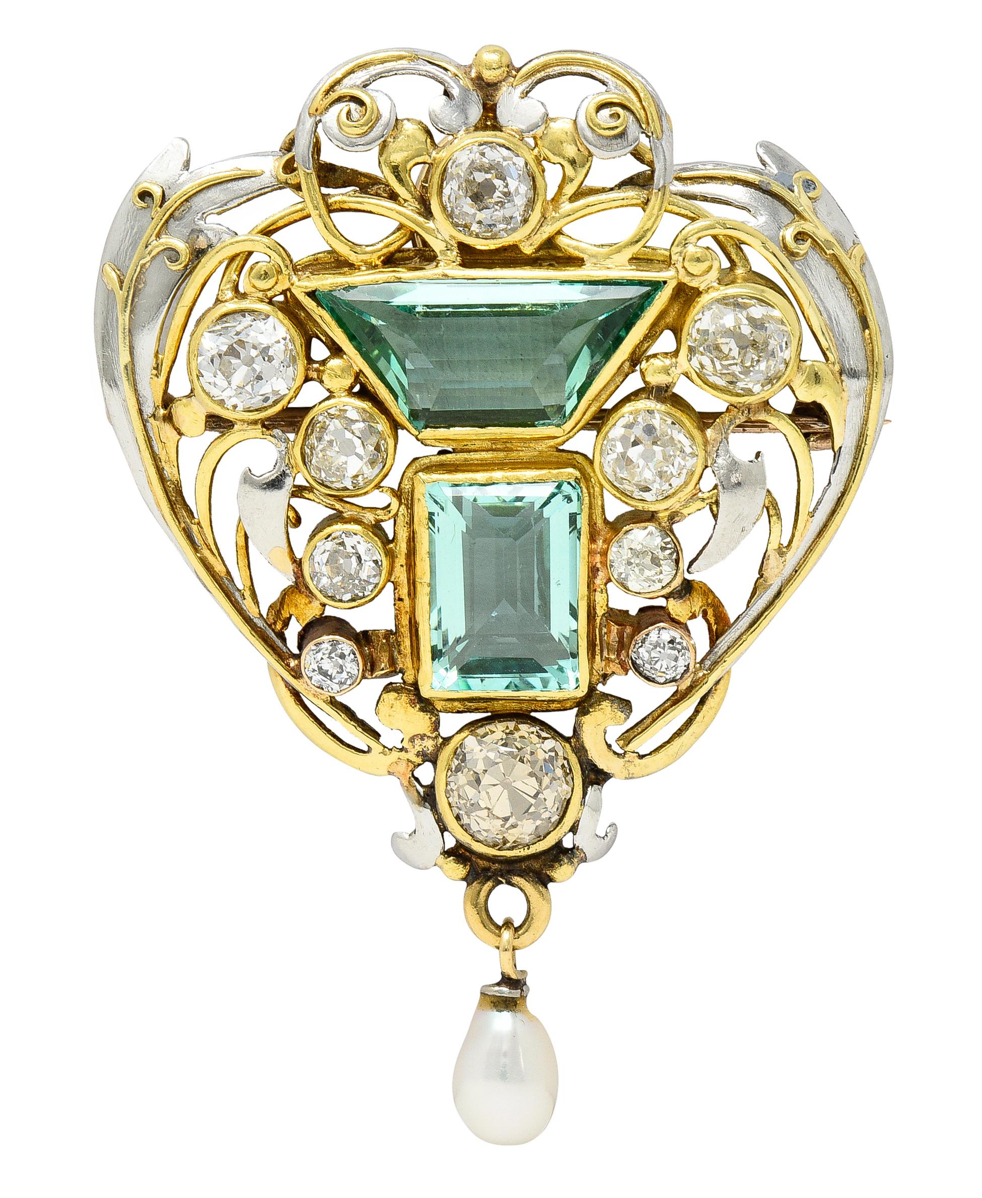 Designed as a platinum and yellow gold pierced foliate motif pendant centering two bezel set emeralds. One is trapezoid-shaped step cut, and the other is an emerald cut - weighing approximately 6.08 carats total. Transparent light bluish-green in